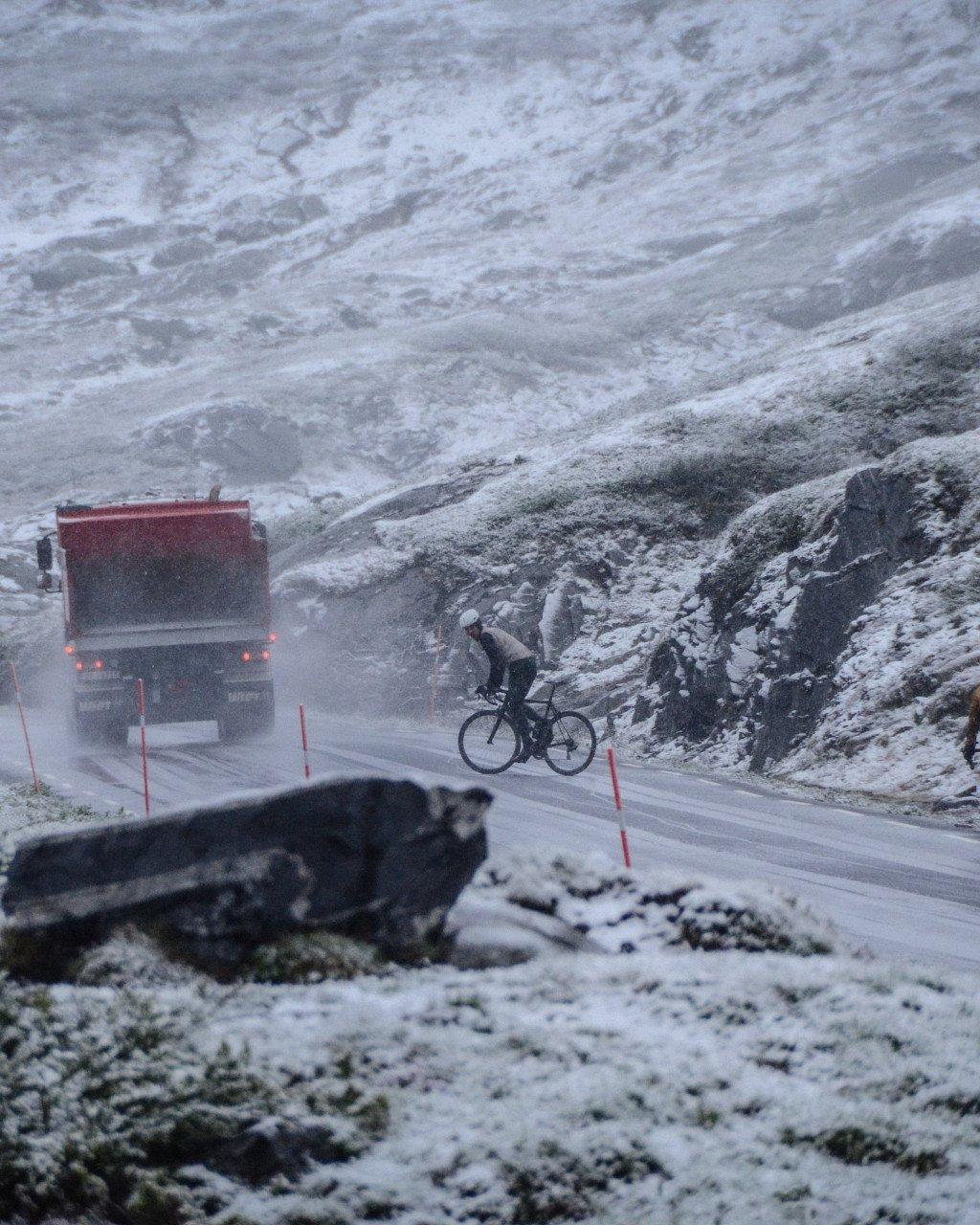 Cyclist riding on snowy mountain road with truck in harsh winter conditions