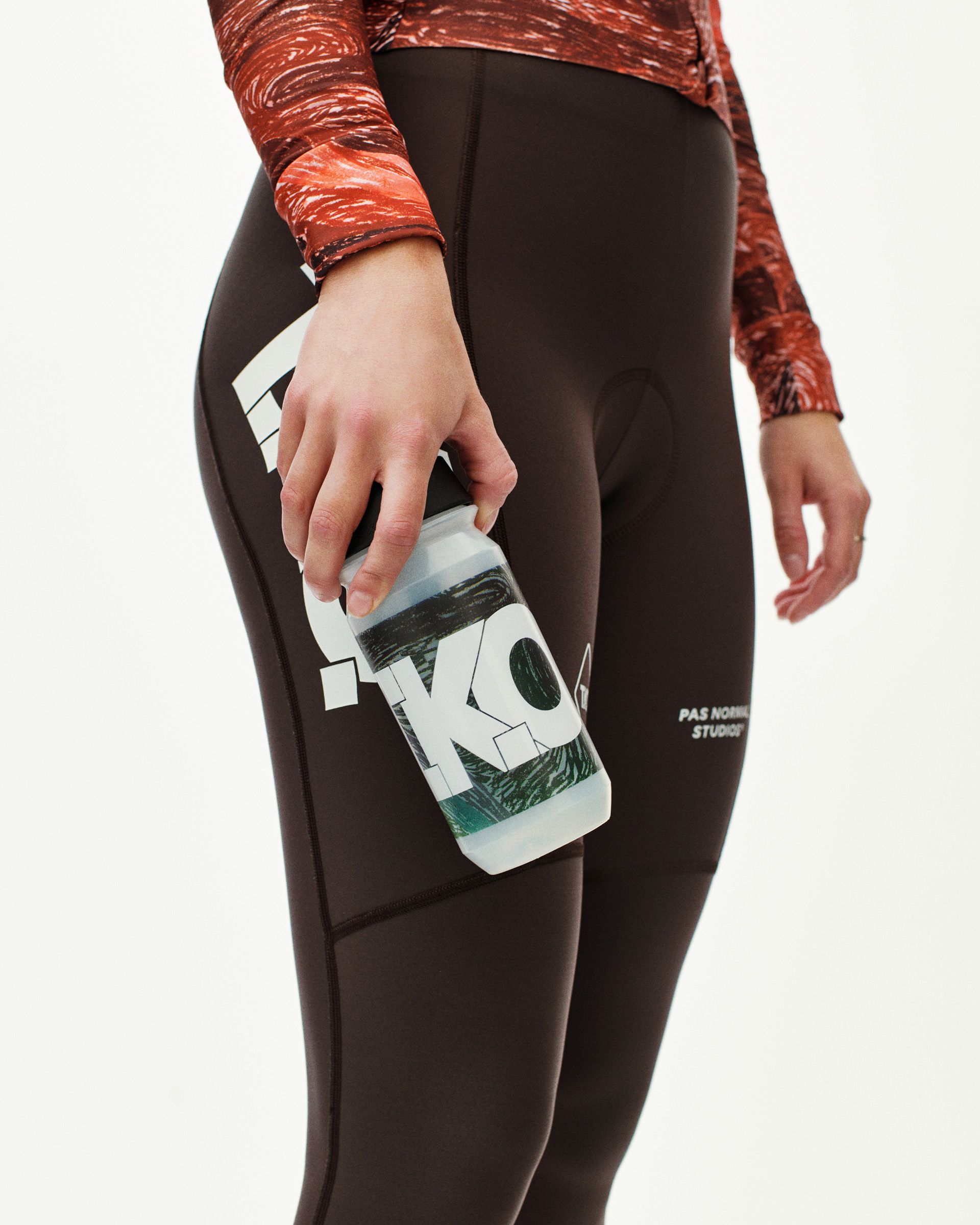 Dark Multi T.K.O. cycling water bottle held by model wearing dark cycling tights, side detail view