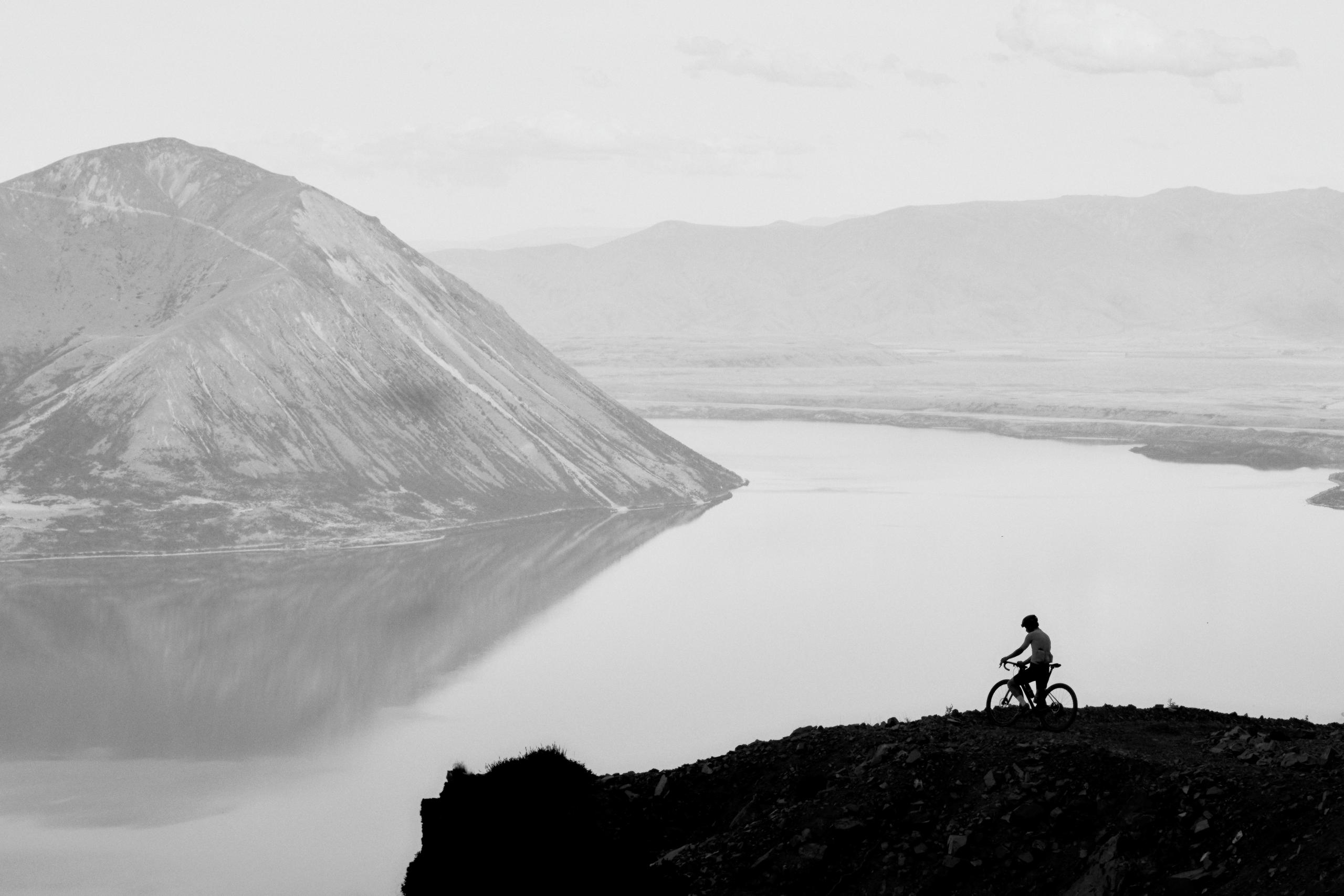 Cyclist silhouetted against mountain lake landscape in black and white