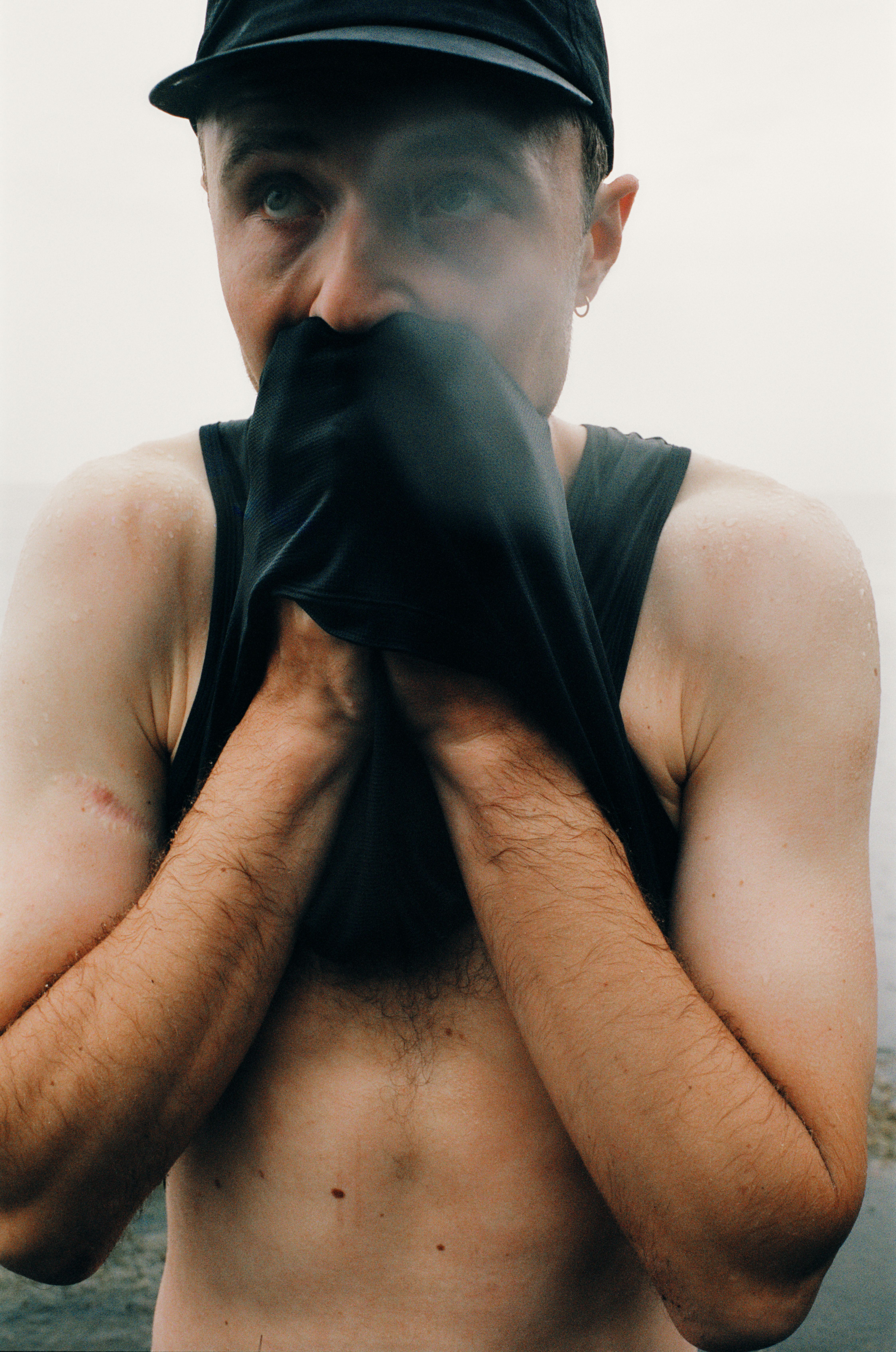 Model wearing black cycling cap with face covering, hands positioned near face