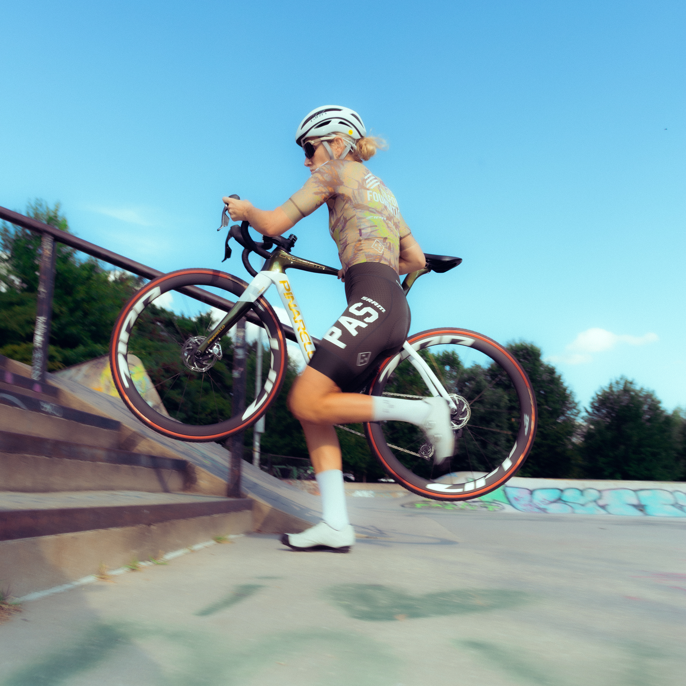 Model wearing multicolored jersey and dark shorts cycling in skate park