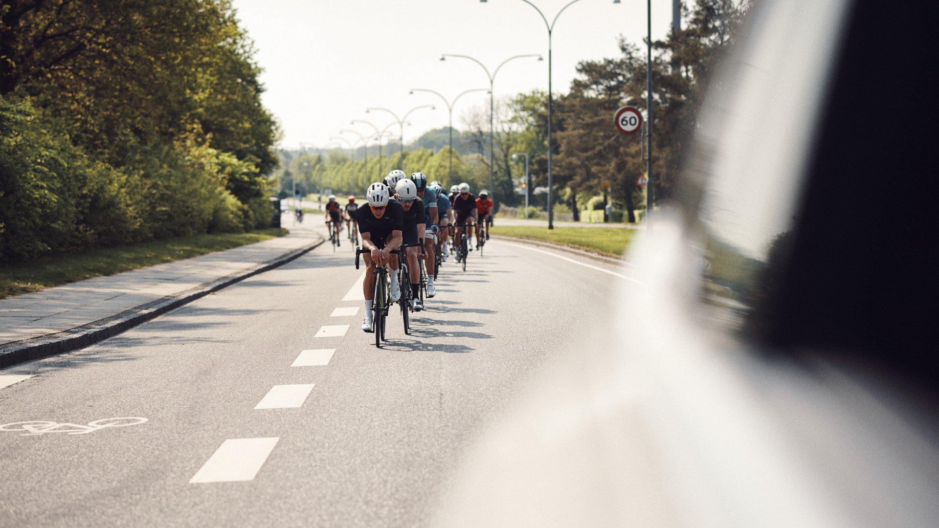 Cyclists in road racing formation on tree-lined road shot from behind vehicle