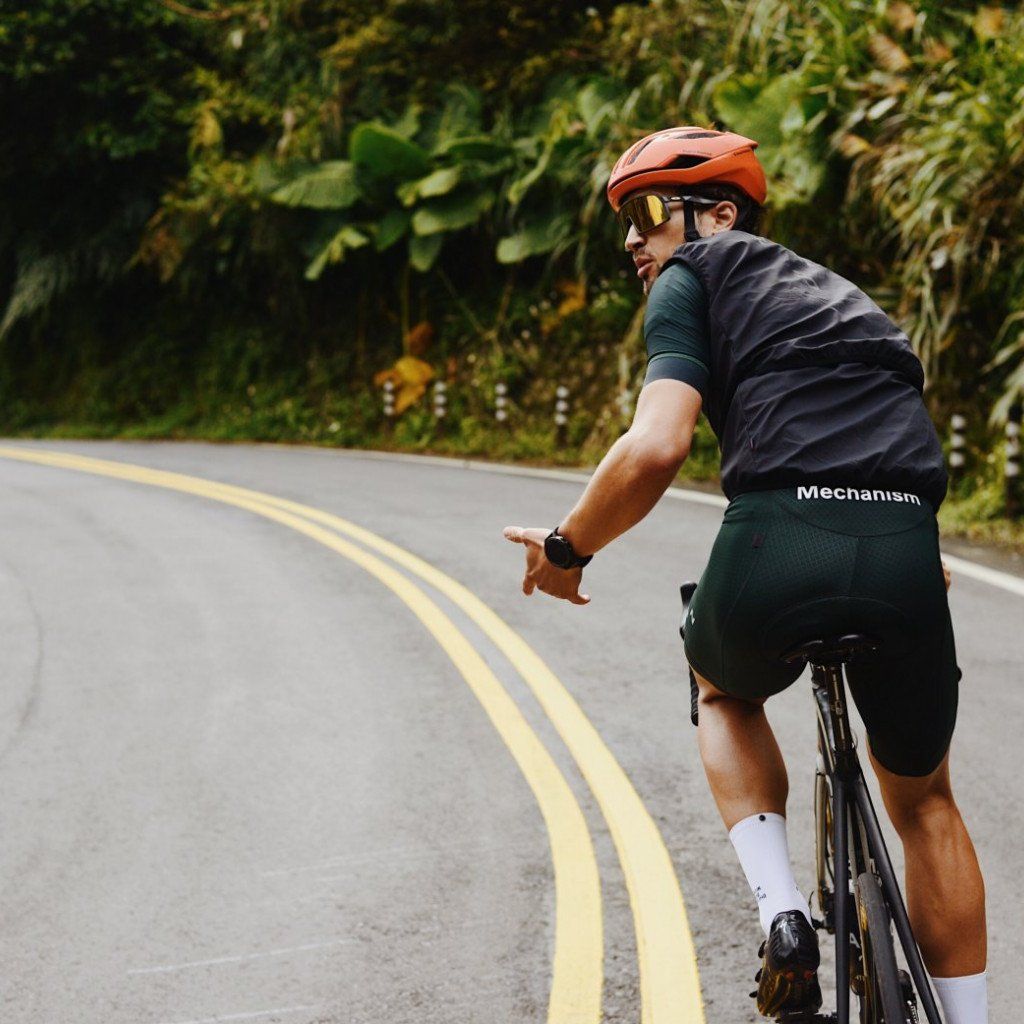 Model wearing Mechanism dark grey jersey and green shorts cycling on road