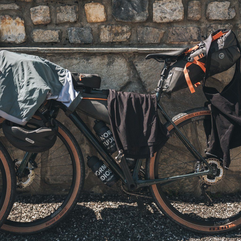 Gravel bike with bags and cycling gear against cobblestone wall, ready for bikepacking adventure