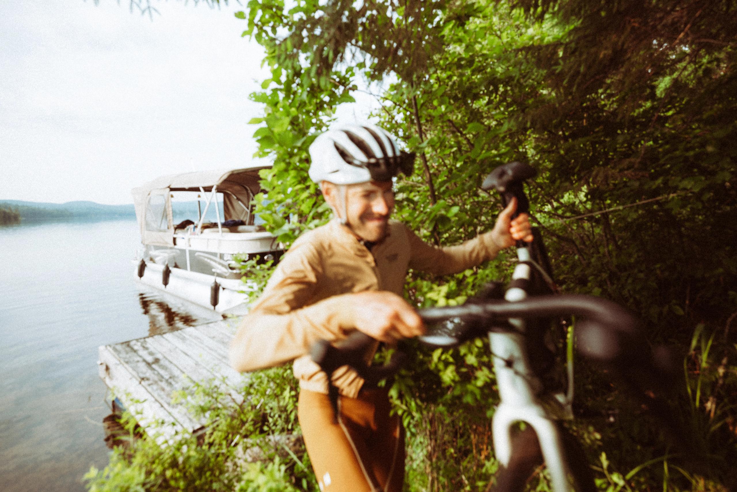 Model wearing tan jersey and white helmet with bike by lakeside dock