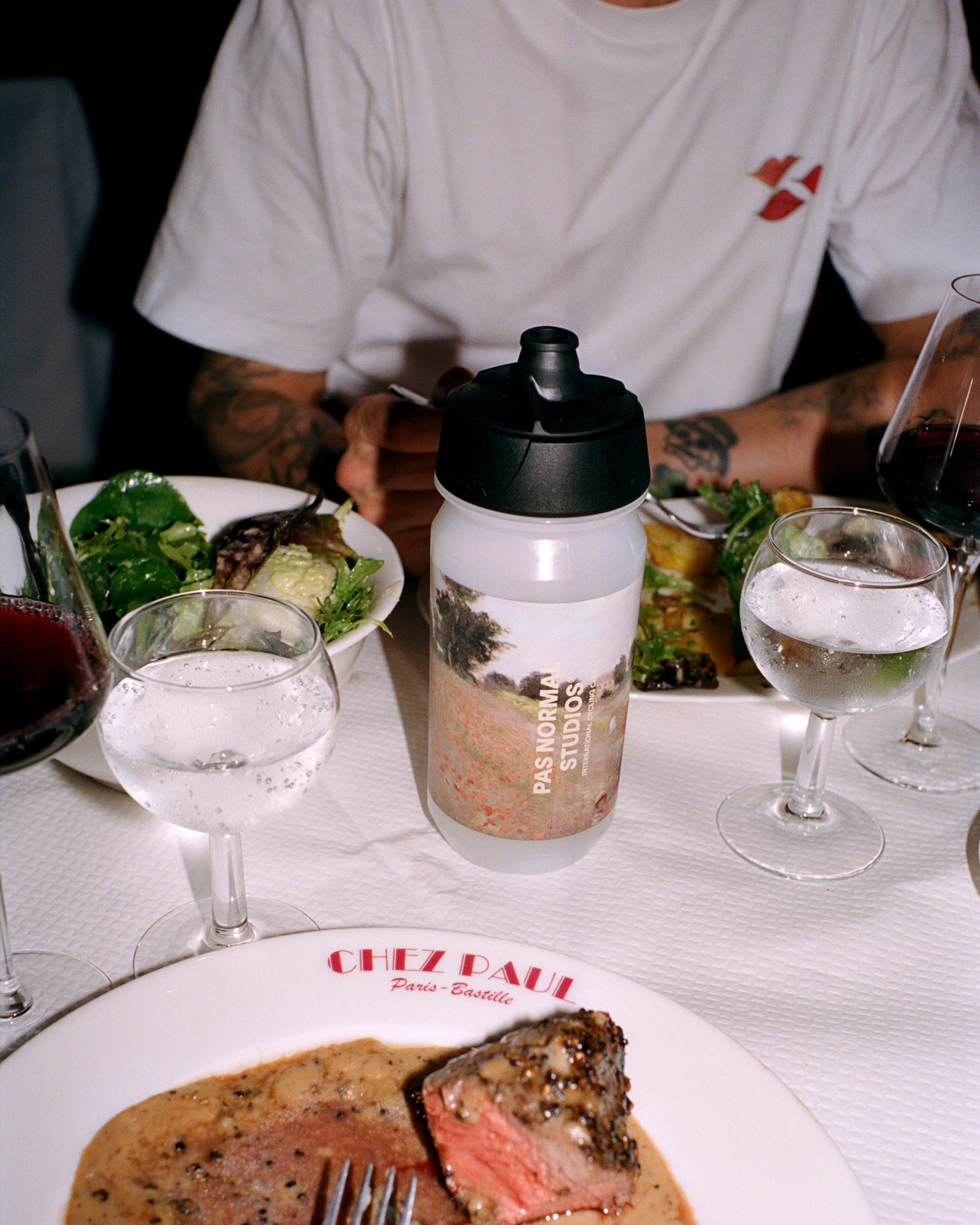 White cycling water bottle with landscape graphic on restaurant table with food and wine glasses