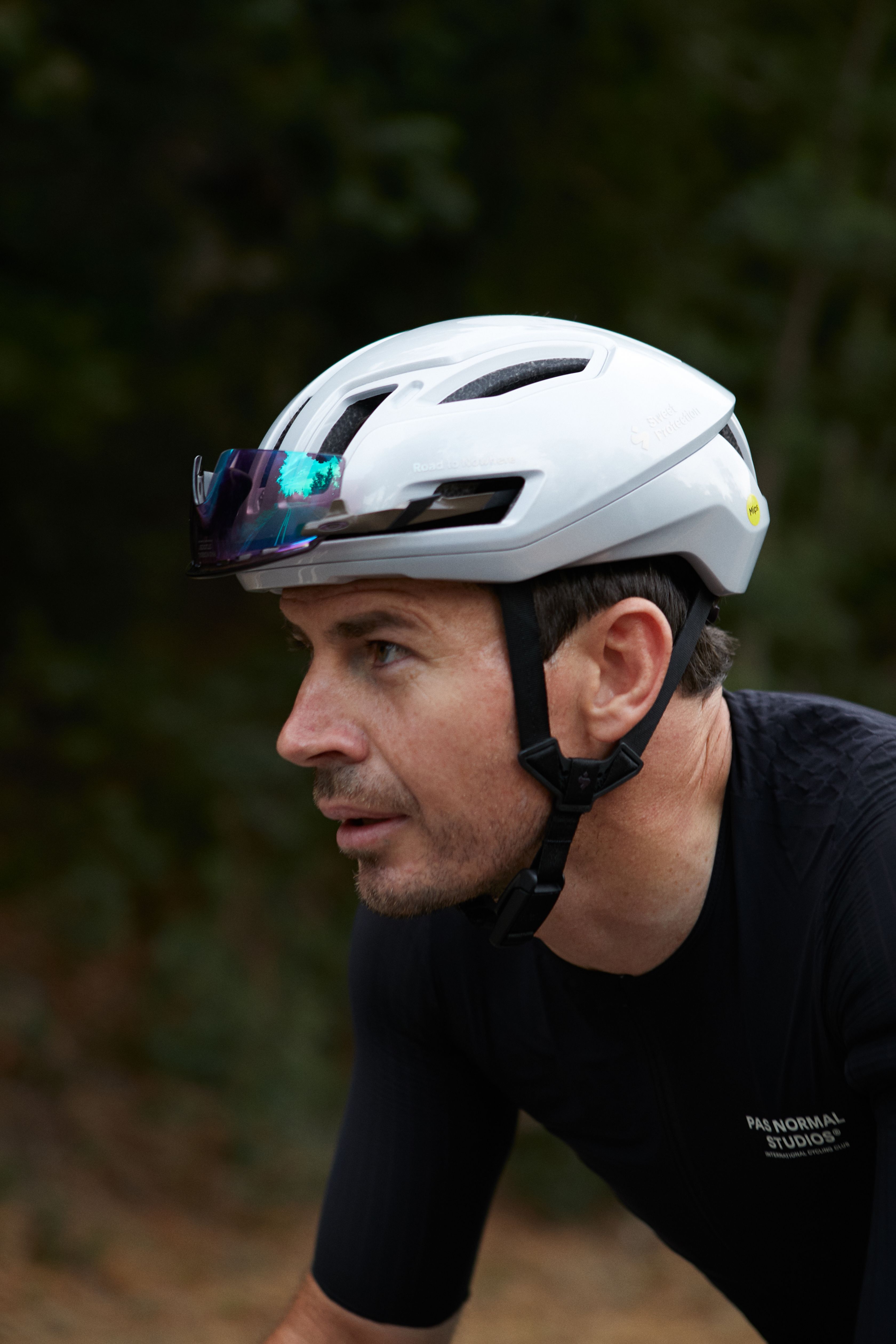 Model wearing white aerodynamic cycling helmet with iridescent visor and black jersey outdoors