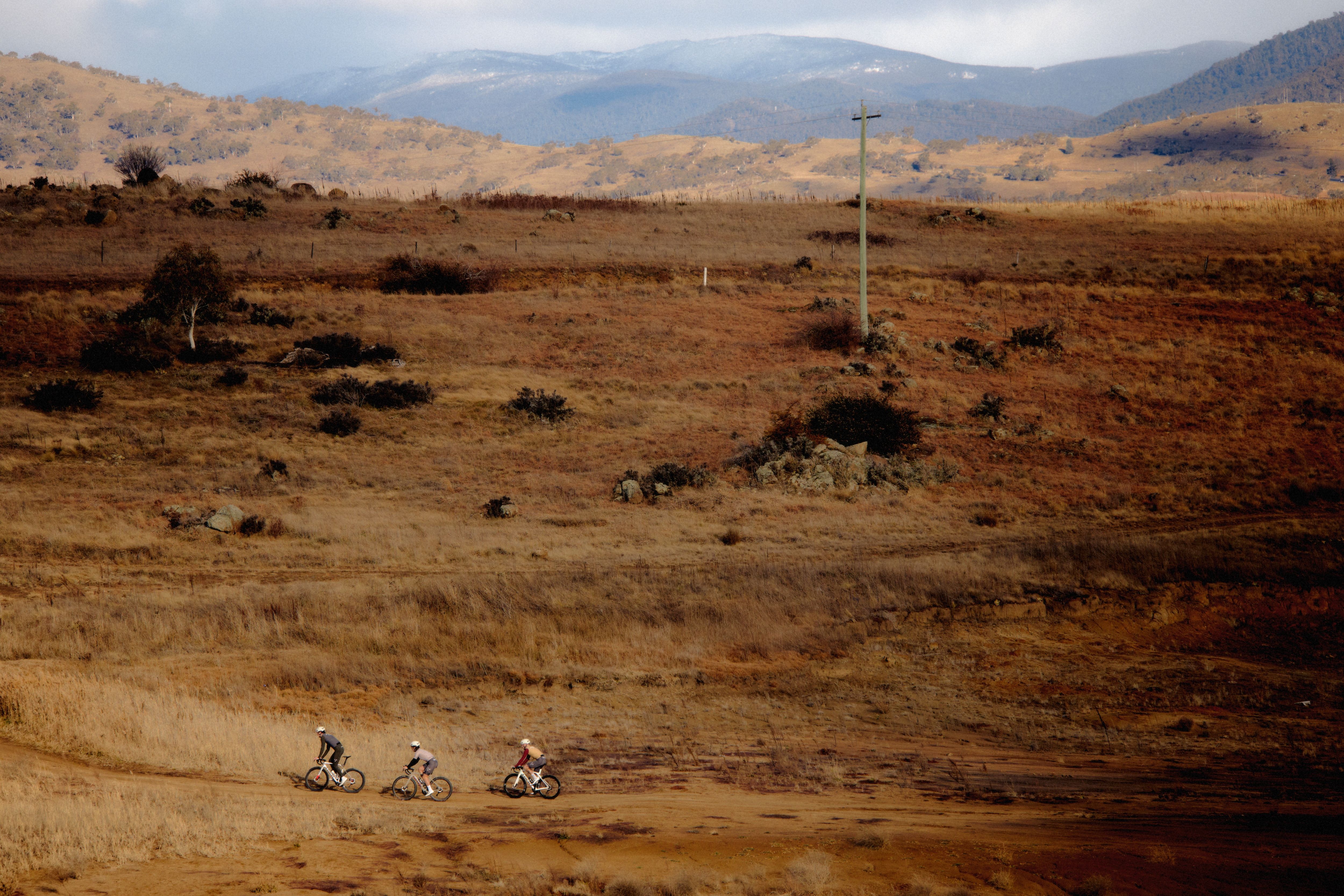 Three cyclists riding through golden autumn landscape with rolling hills and mountains