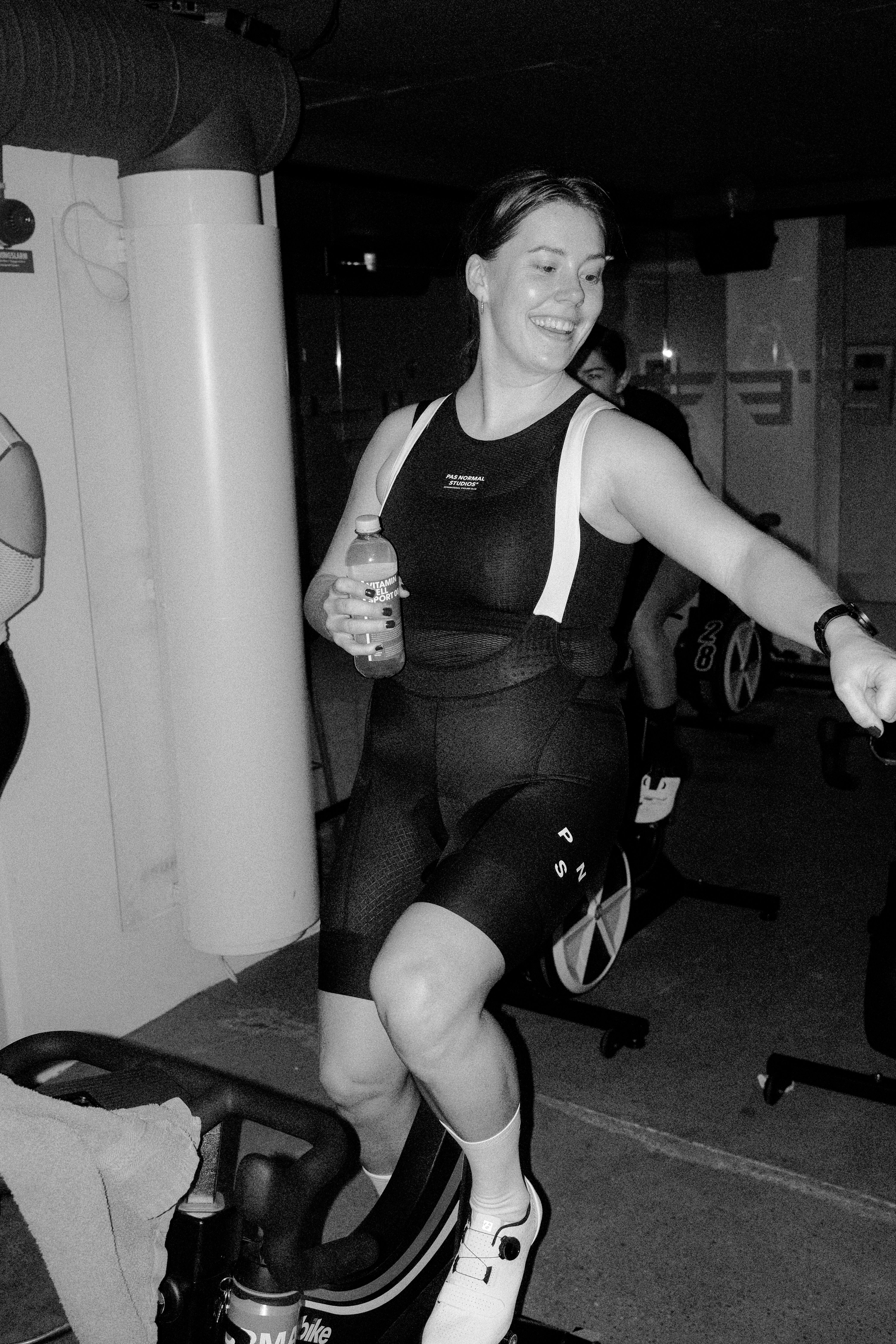 Model wearing black sleeveless cycling bodysuit with logo branding in gym setting
