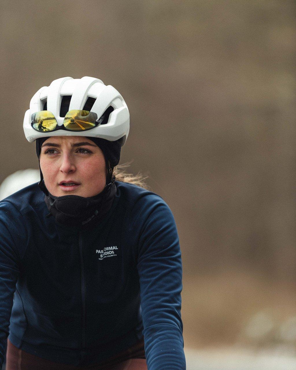 Model wearing navy cycling jacket with chest branding and white helmet with reflective lenses