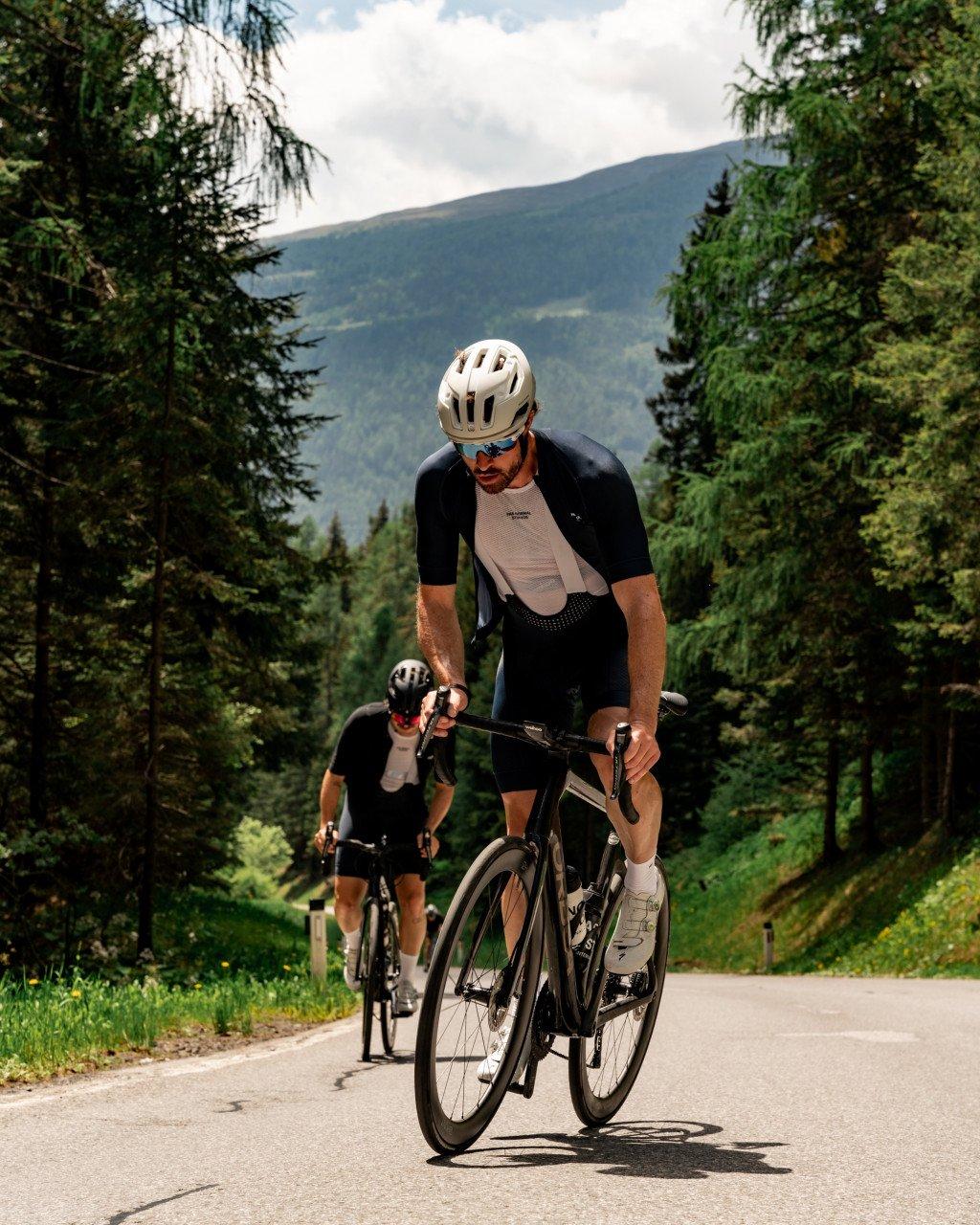 Two cyclists in black and beige cycling kit riding time trial bikes on mountain road