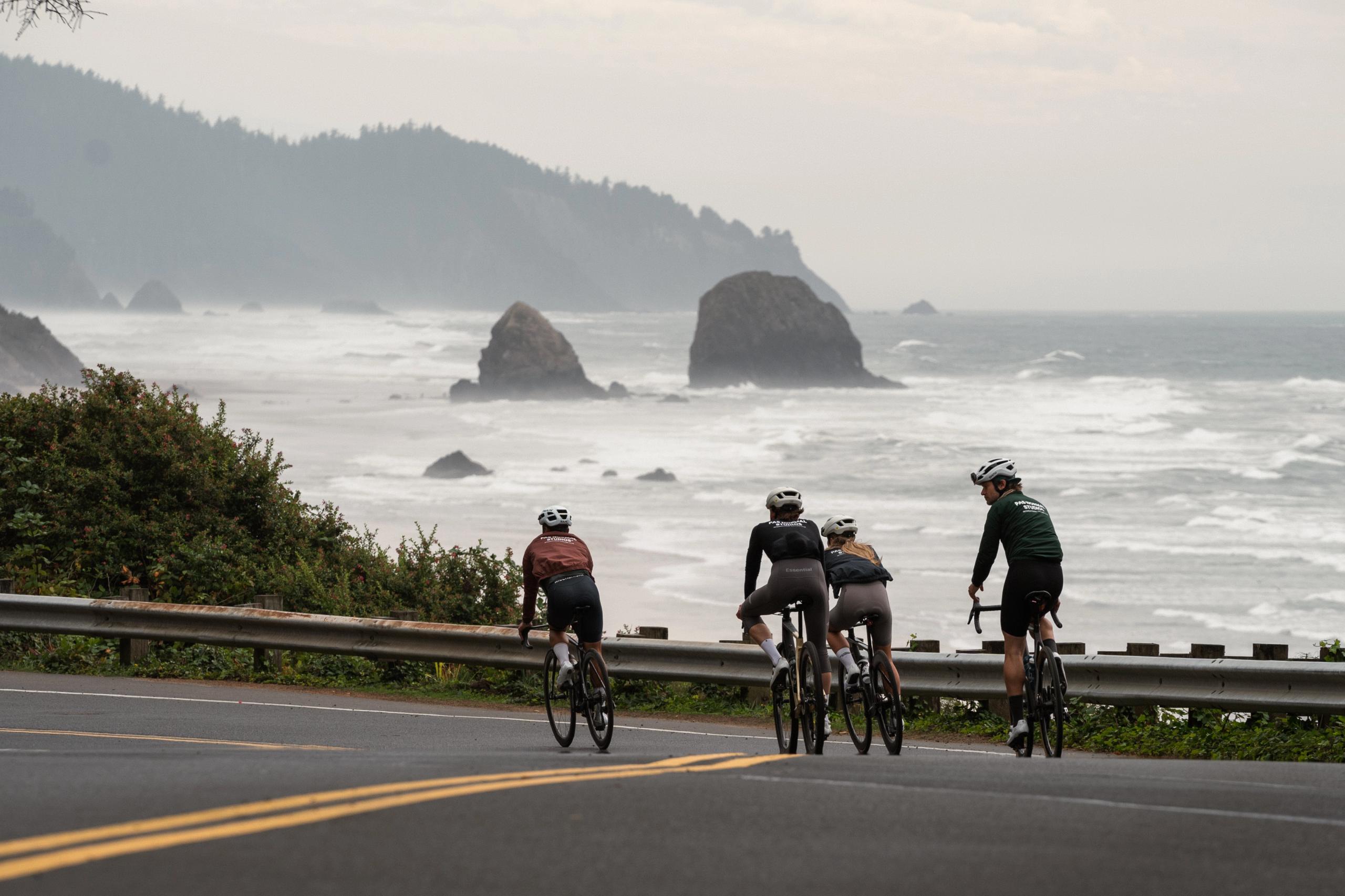 Cyclists in colorful jerseys riding along coastal road with ocean and rock formations in background