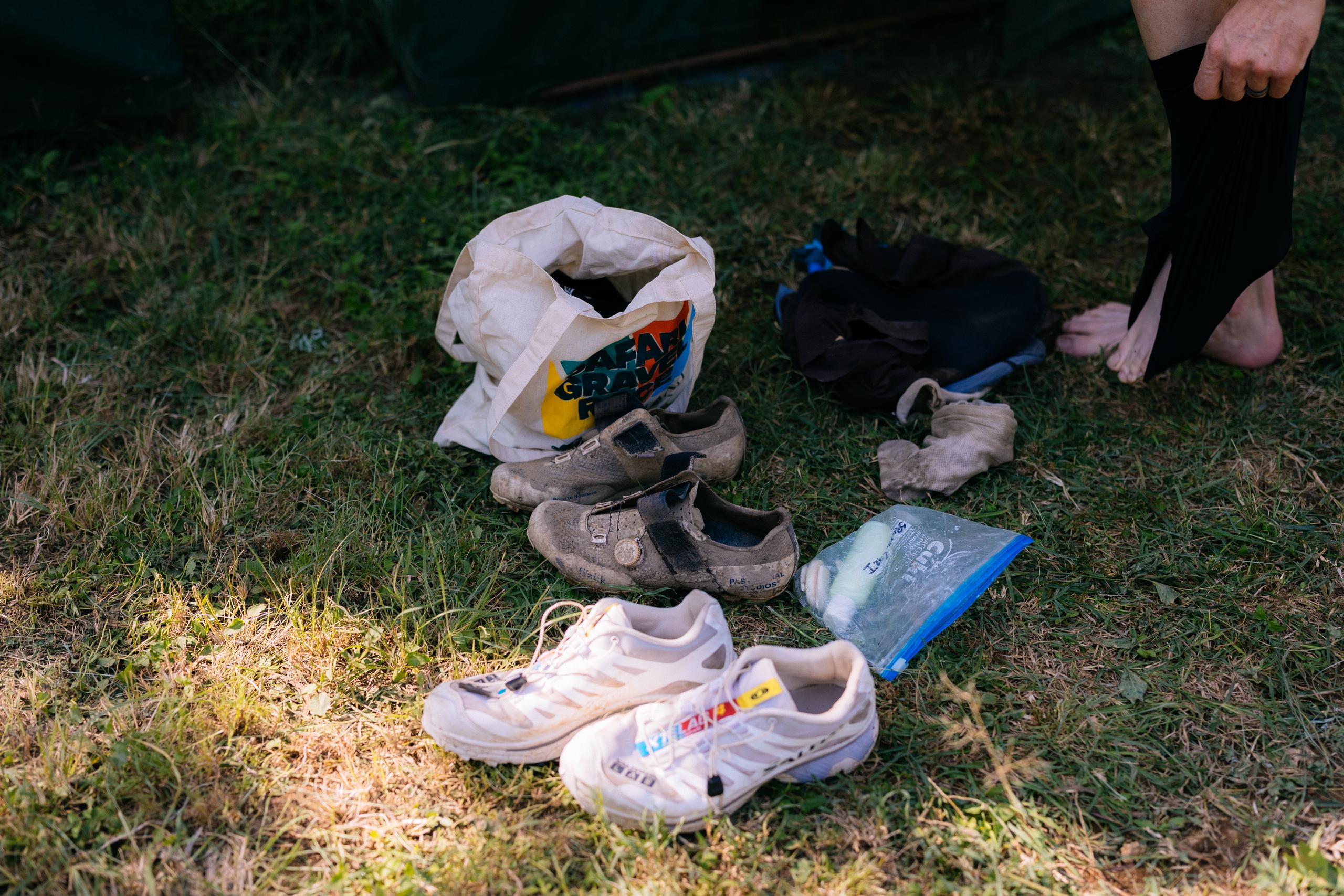 Cycling gear and shoes scattered on grass after gravel race with tote bag and water bottle