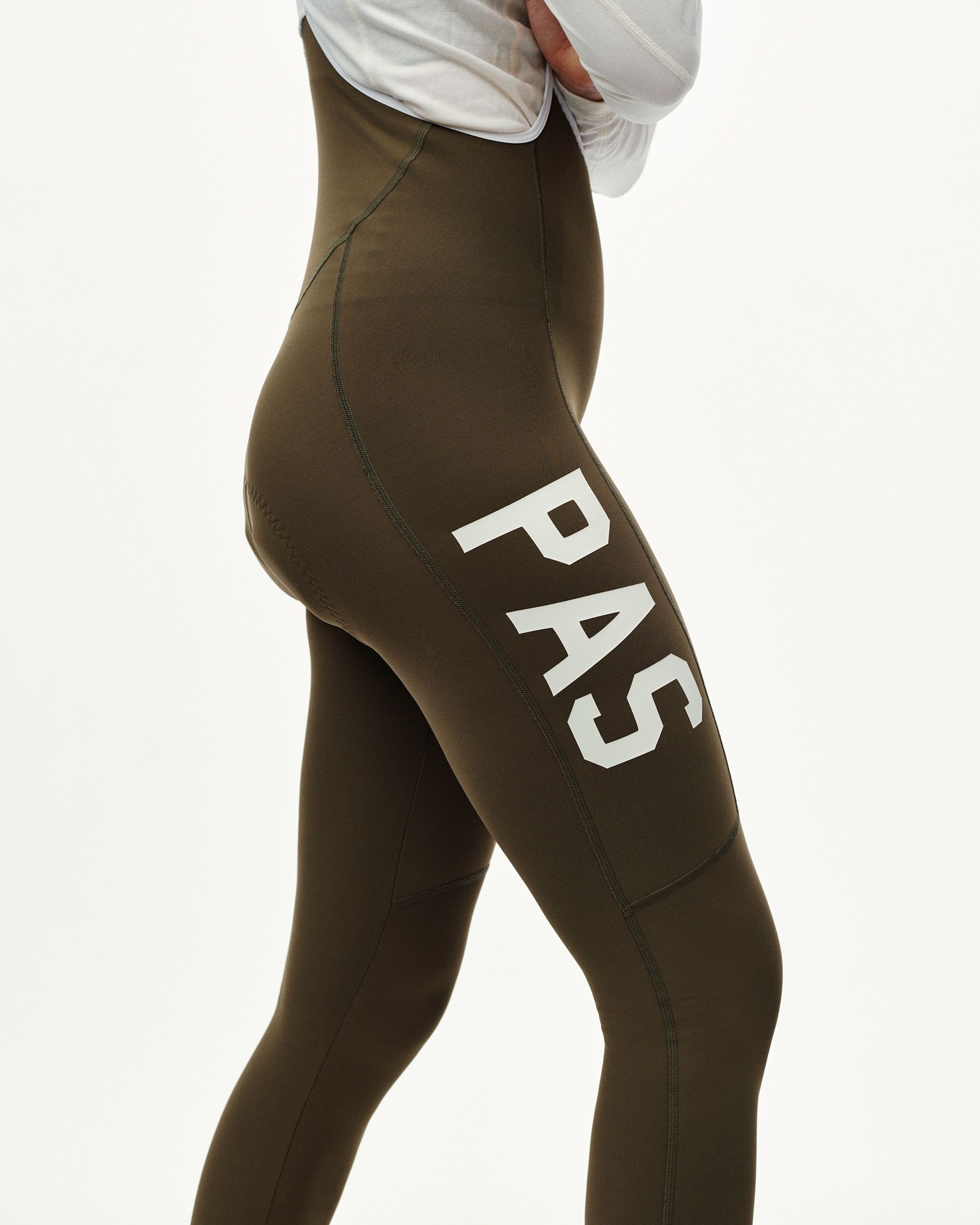 Dark Earth khaki PAS Mechanism Thermal Long cycling bibs on model, side view with white PAS leg print