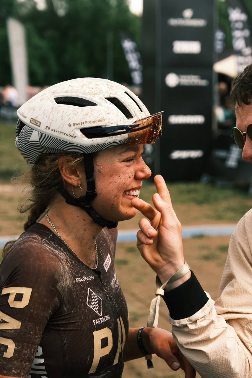 Model wearing muddy cycling jersey with large logo lettering after race, white helmet with visor
