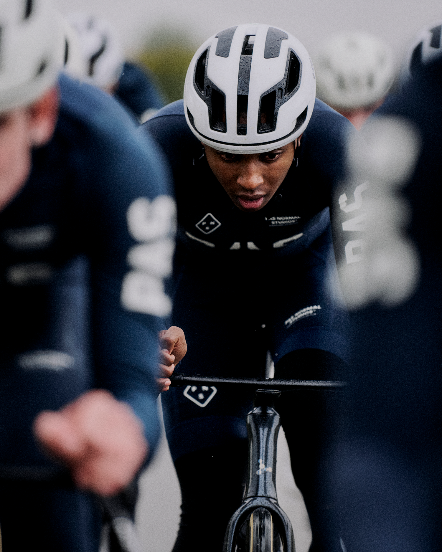 Model wearing black cycling skinsuit with white helmet in aerodynamic position on time trial bike