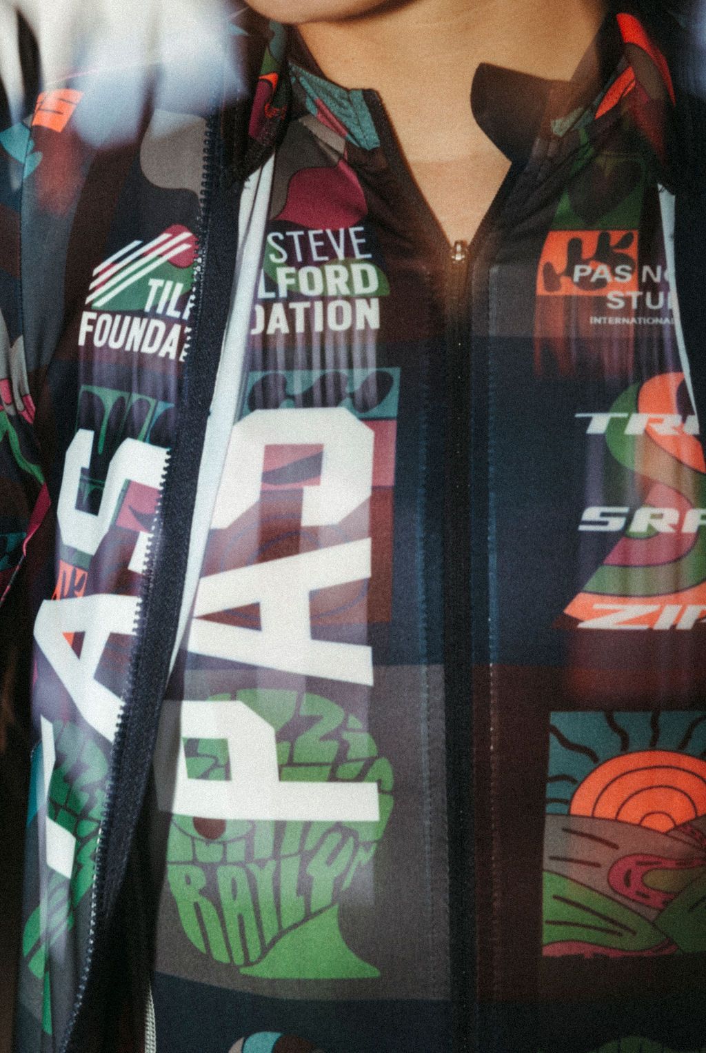 Model wearing multicolored cycling jacket with collage-style graphic print and full zip