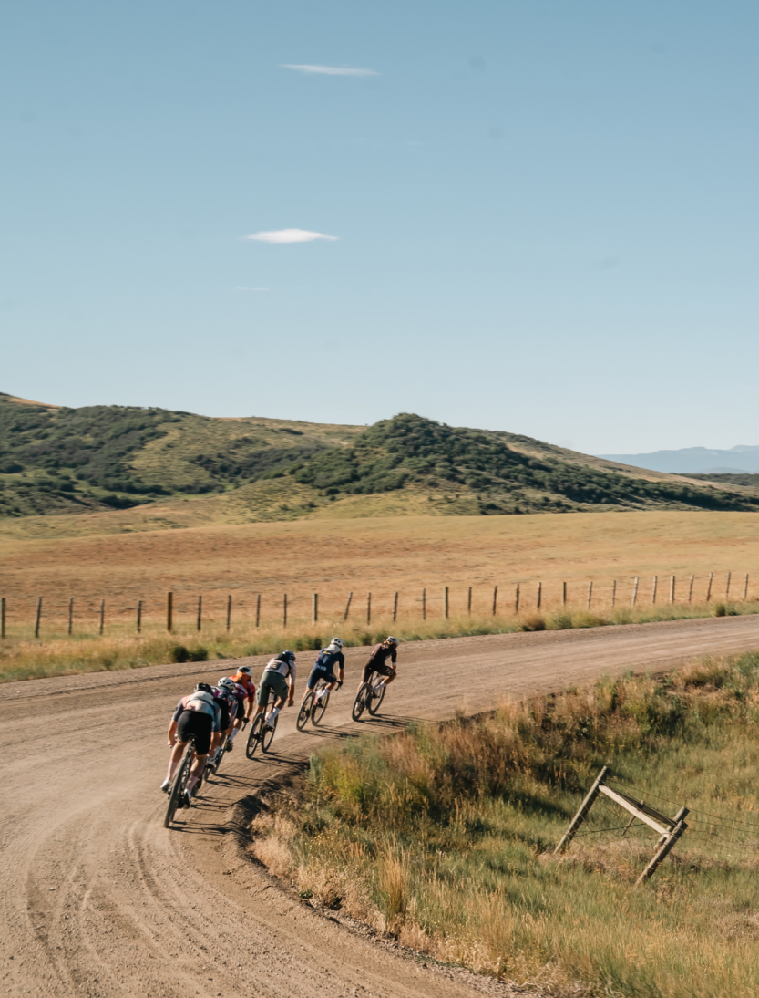 Cyclists riding on gravel road through rural countryside with rolling hills and fence line