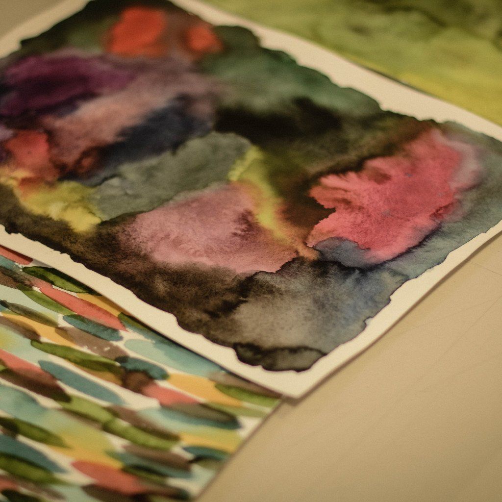 Colorful watercolor paintings stacked on paper showing abstract landscape-like compositions