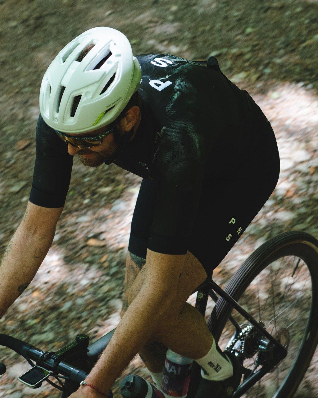 Model wearing black cycling jersey with green detailing and white helmet on gravel bike