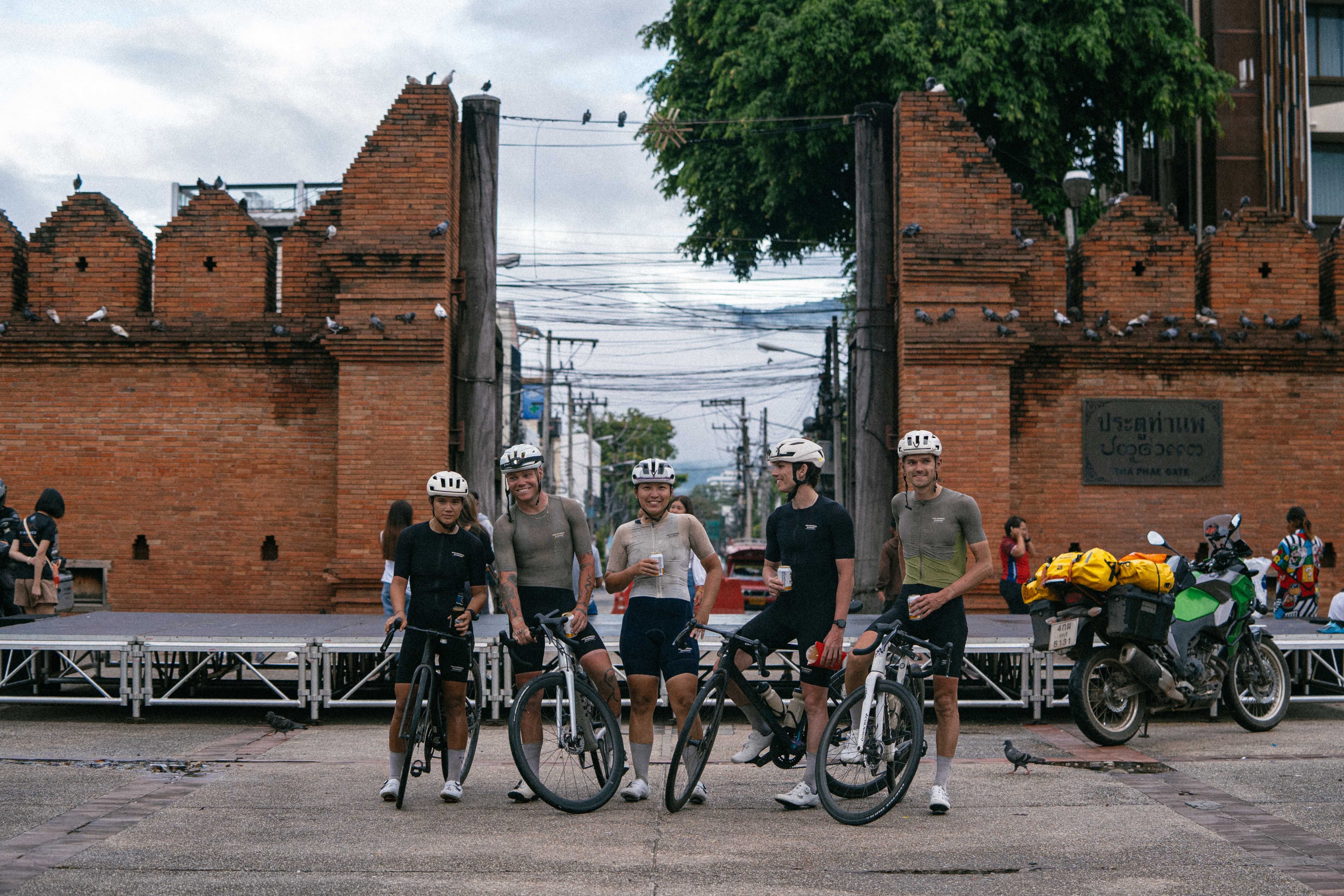 Group of cyclists with bikes posing in front of historic brick gate in Thailand