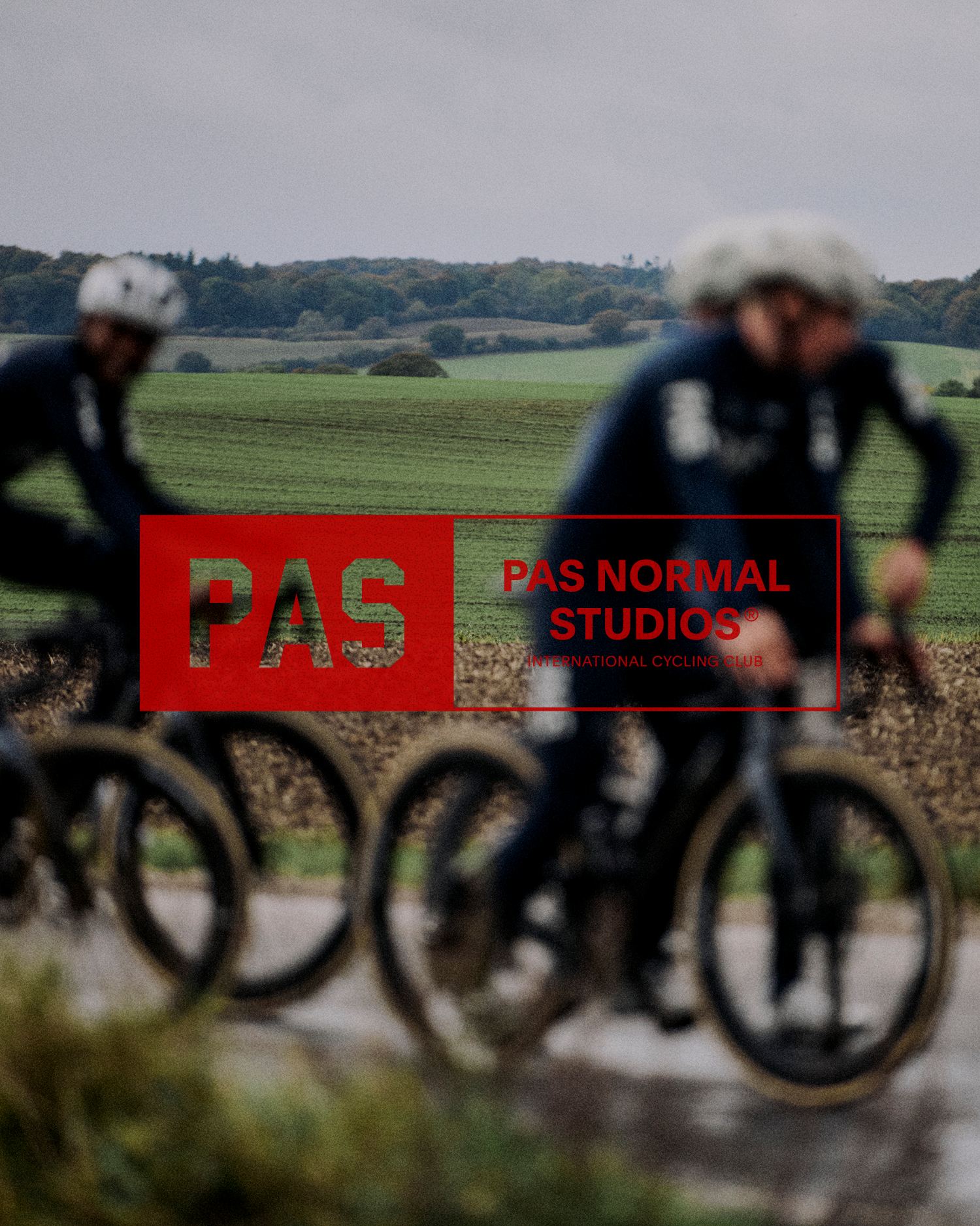 Two cyclists in rural countryside with red logo overlay and rolling hills in background