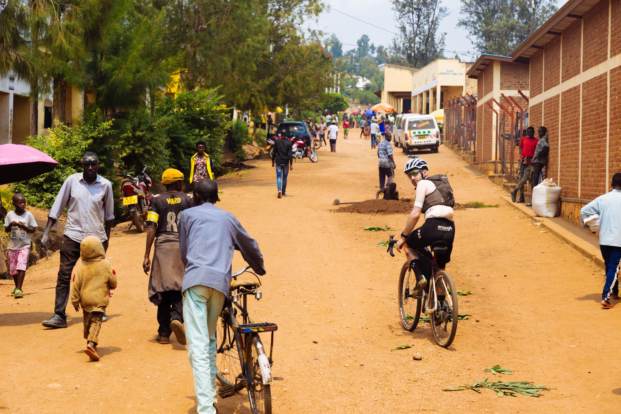 Cyclist in white jersey and black shorts riding through busy street scene in rural town