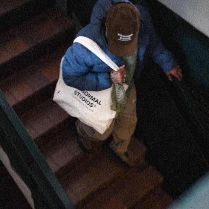 Model wearing blue jacket and brown beanie carrying white tote bag with text on stairs