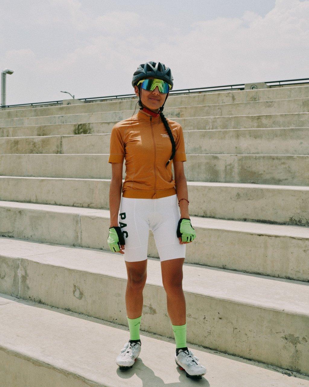 Model wearing orange jersey and white shorts with green gloves and socks, standing on concrete steps