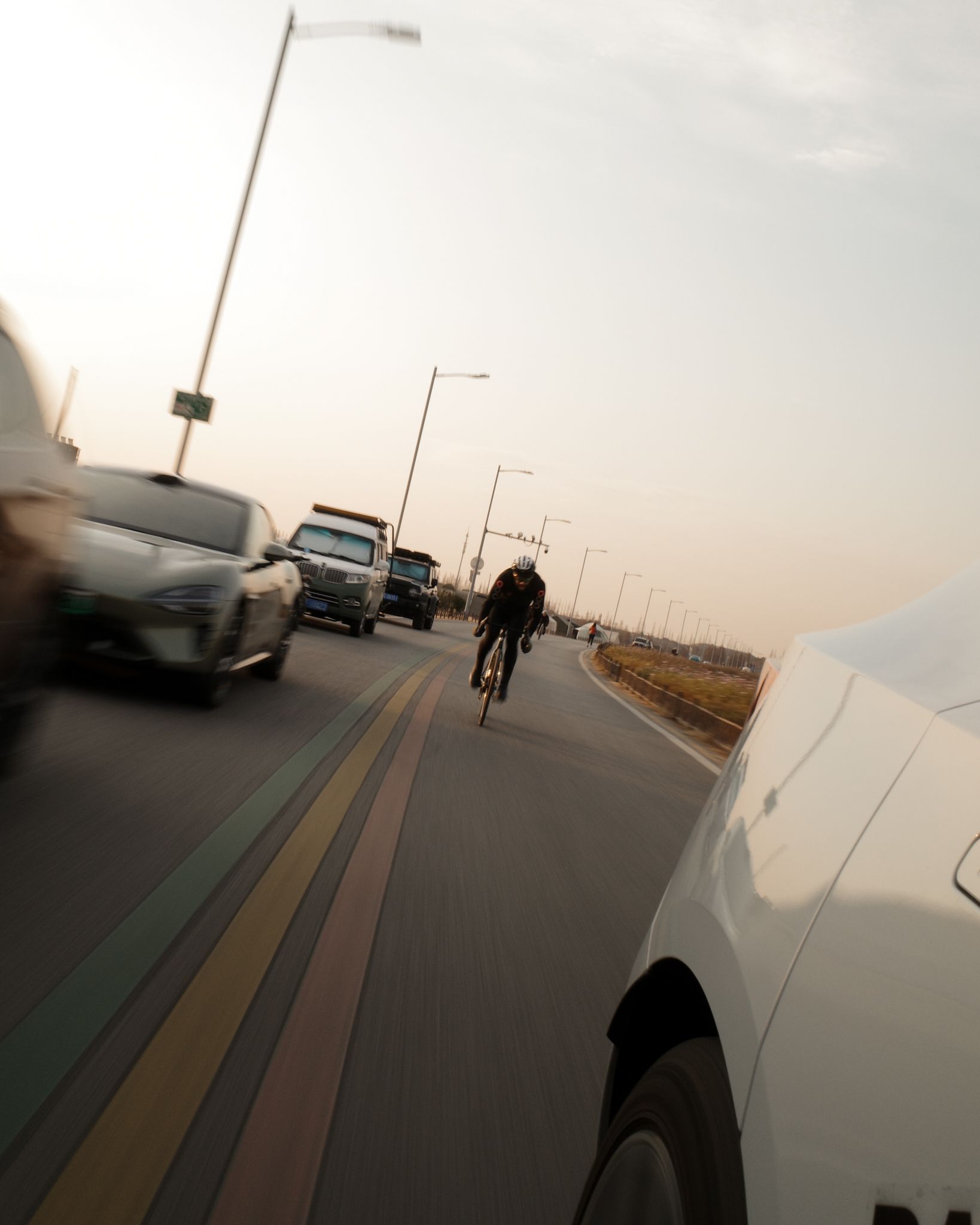 Cyclist in dark clothing riding on road with cars and street lights at dusk