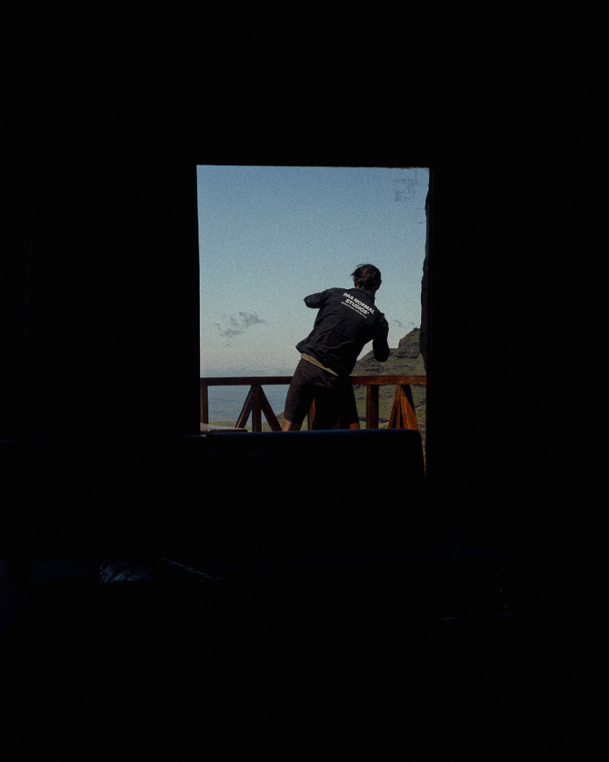 Model wearing black cycling jersey viewed through window frame in mountainous landscape
