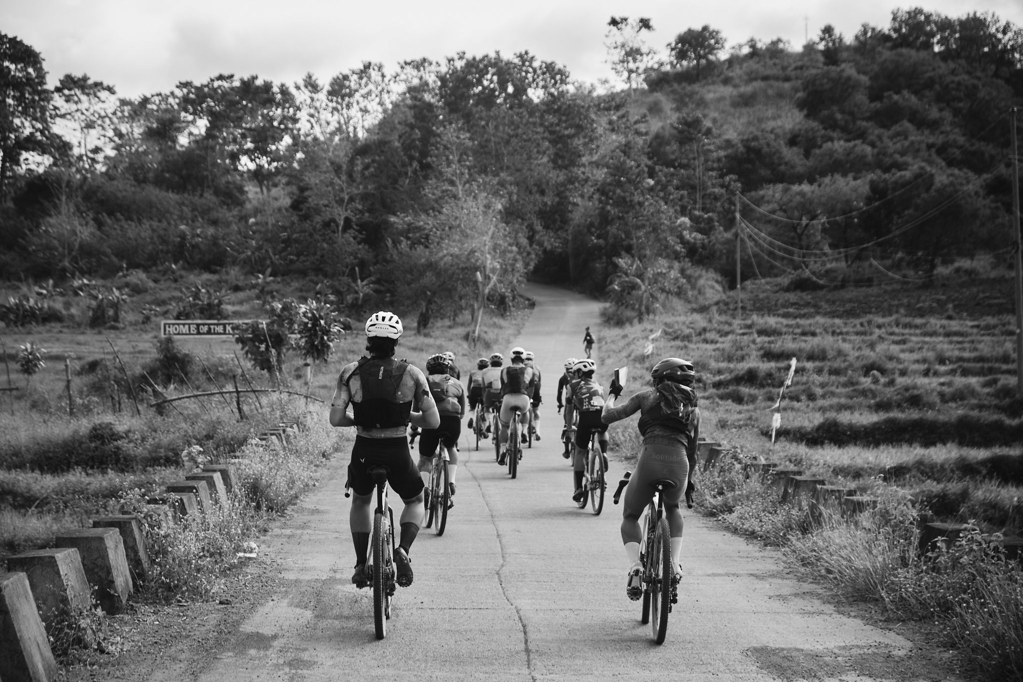 Group of cyclists riding on rural road through hilly countryside in black and white