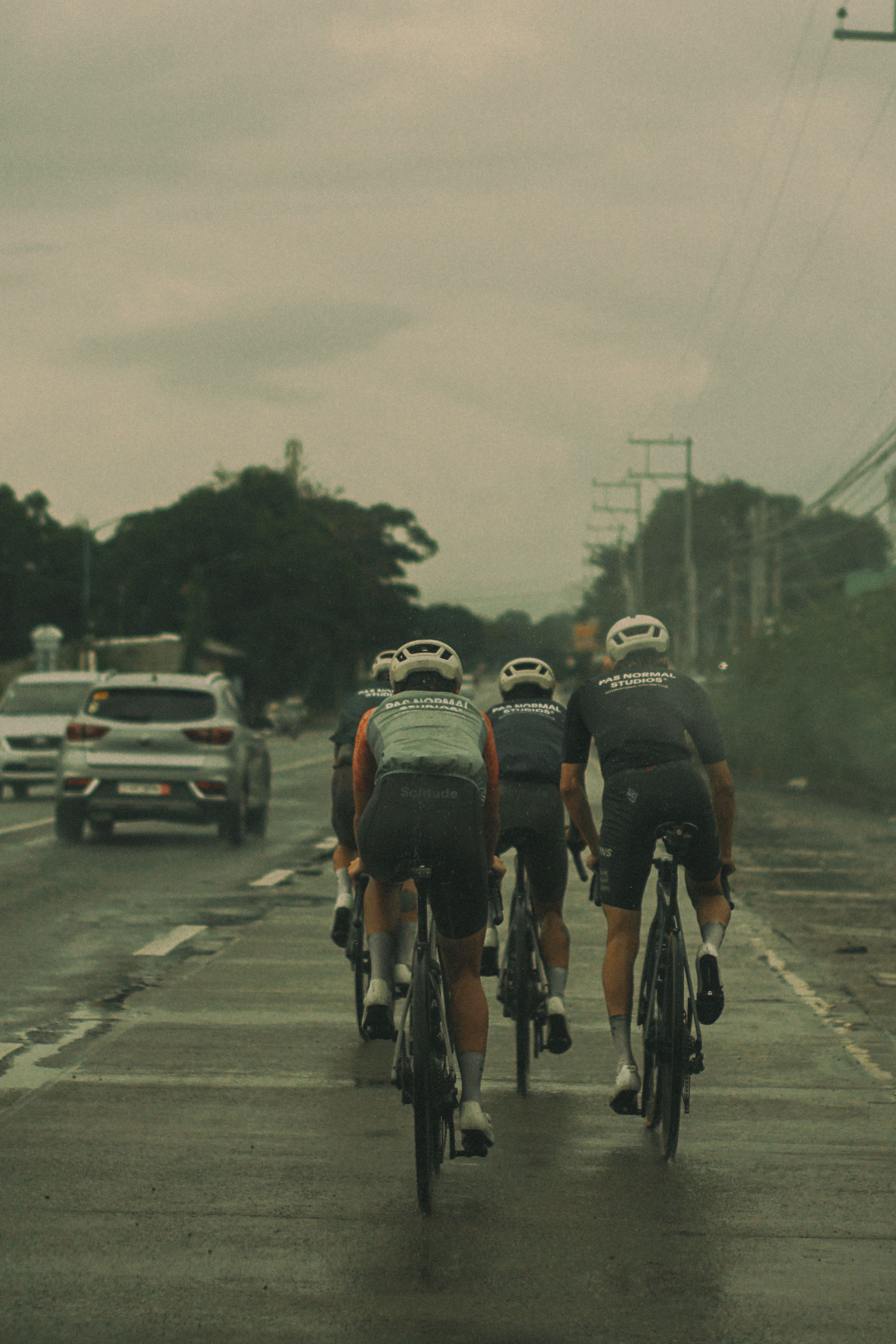 Three cyclists riding in aerodynamic position on road wearing cycling jerseys and helmets
