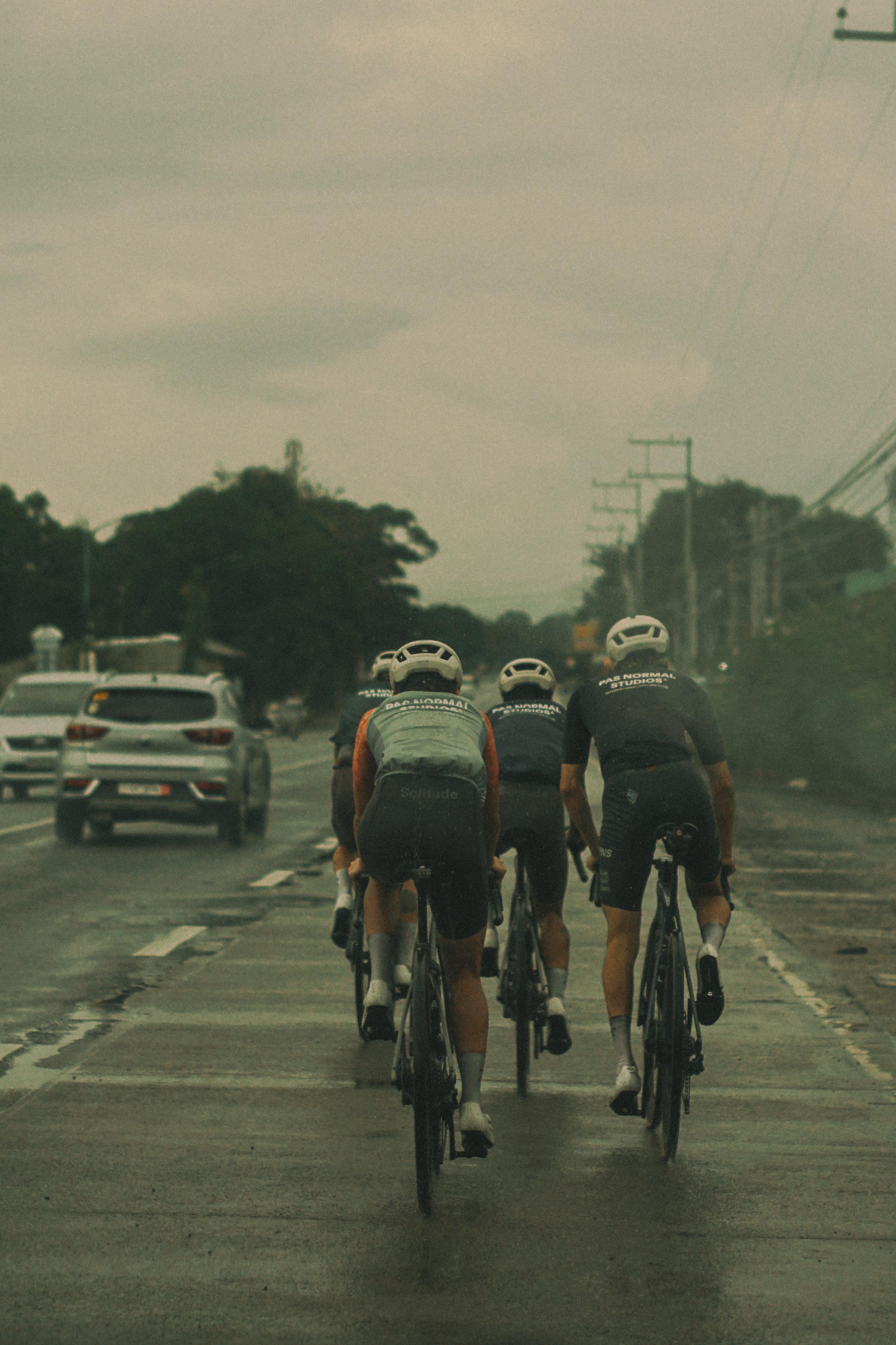 Three cyclists riding in aerodynamic position on road wearing cycling jerseys and helmets