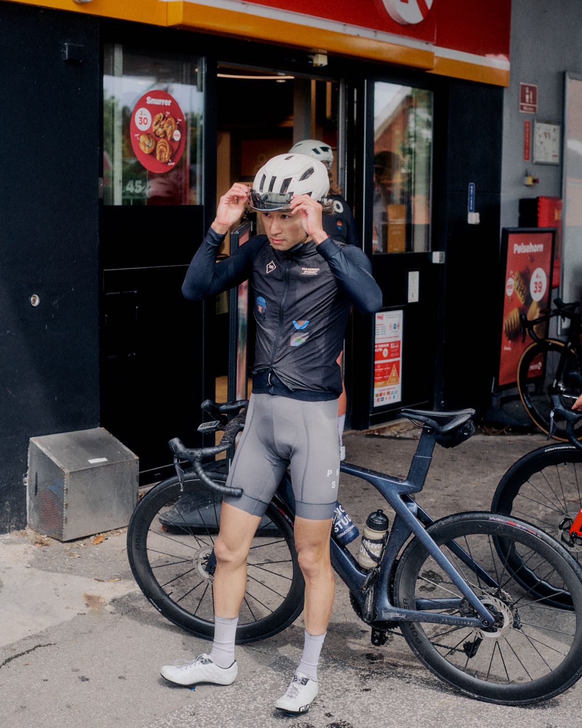 Cyclist adjusting helmet wearing dark long-sleeve jersey and grey shorts next to time trial bike