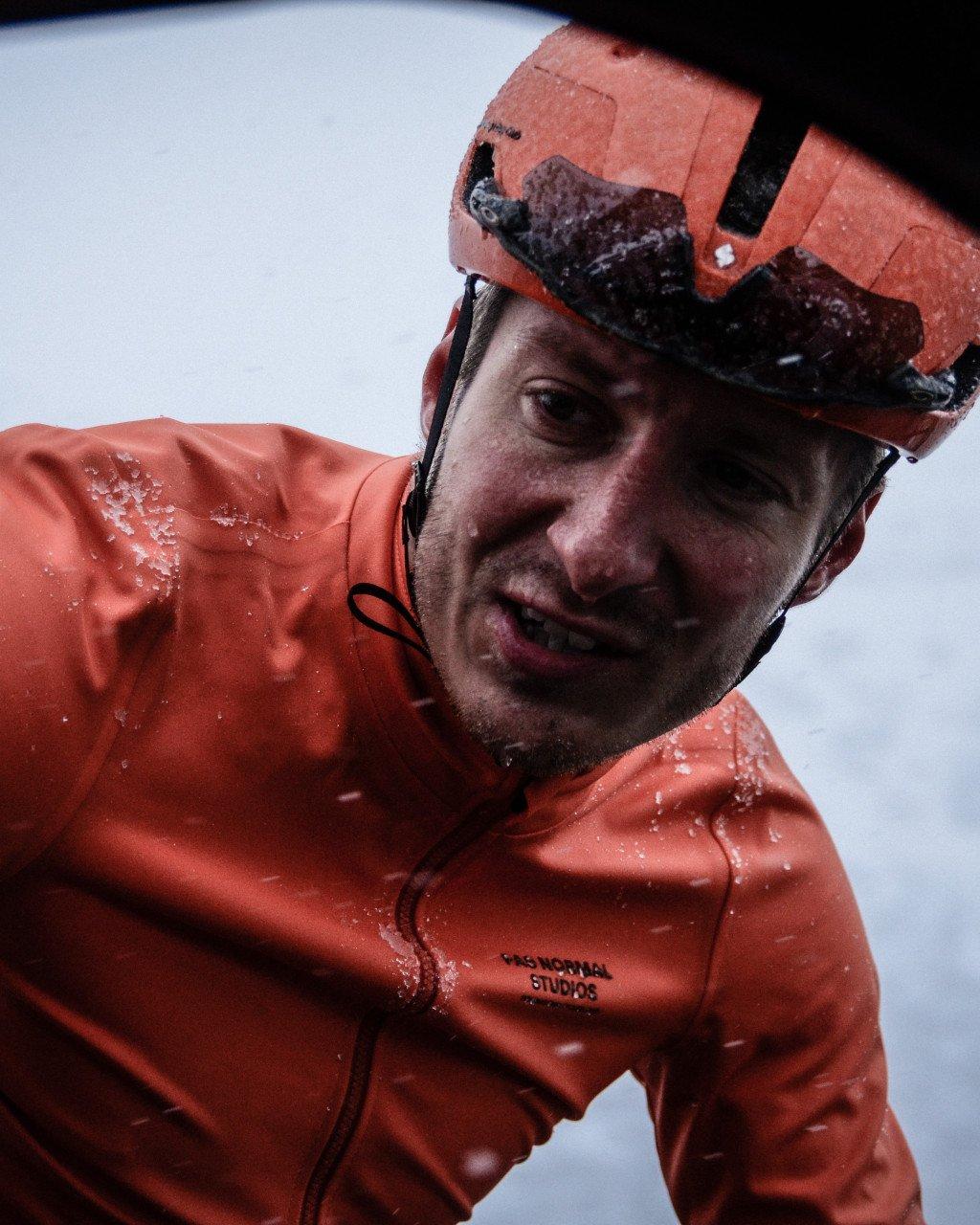 Model wearing orange rain jacket with chest branding and orange helmet in wet conditions