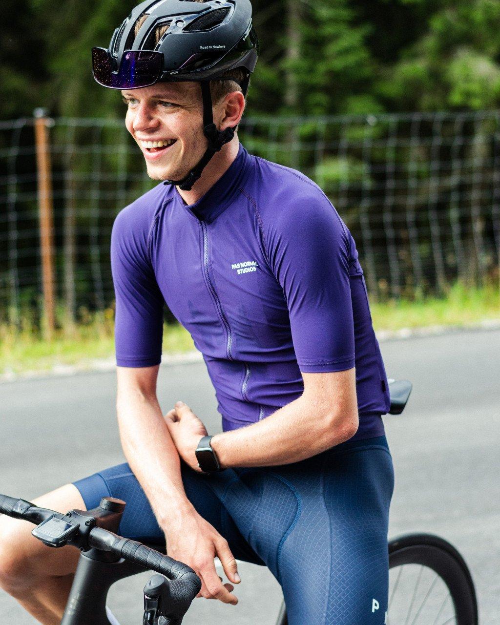 Model wearing purple cycling jersey and dark blue shorts on time trial bike