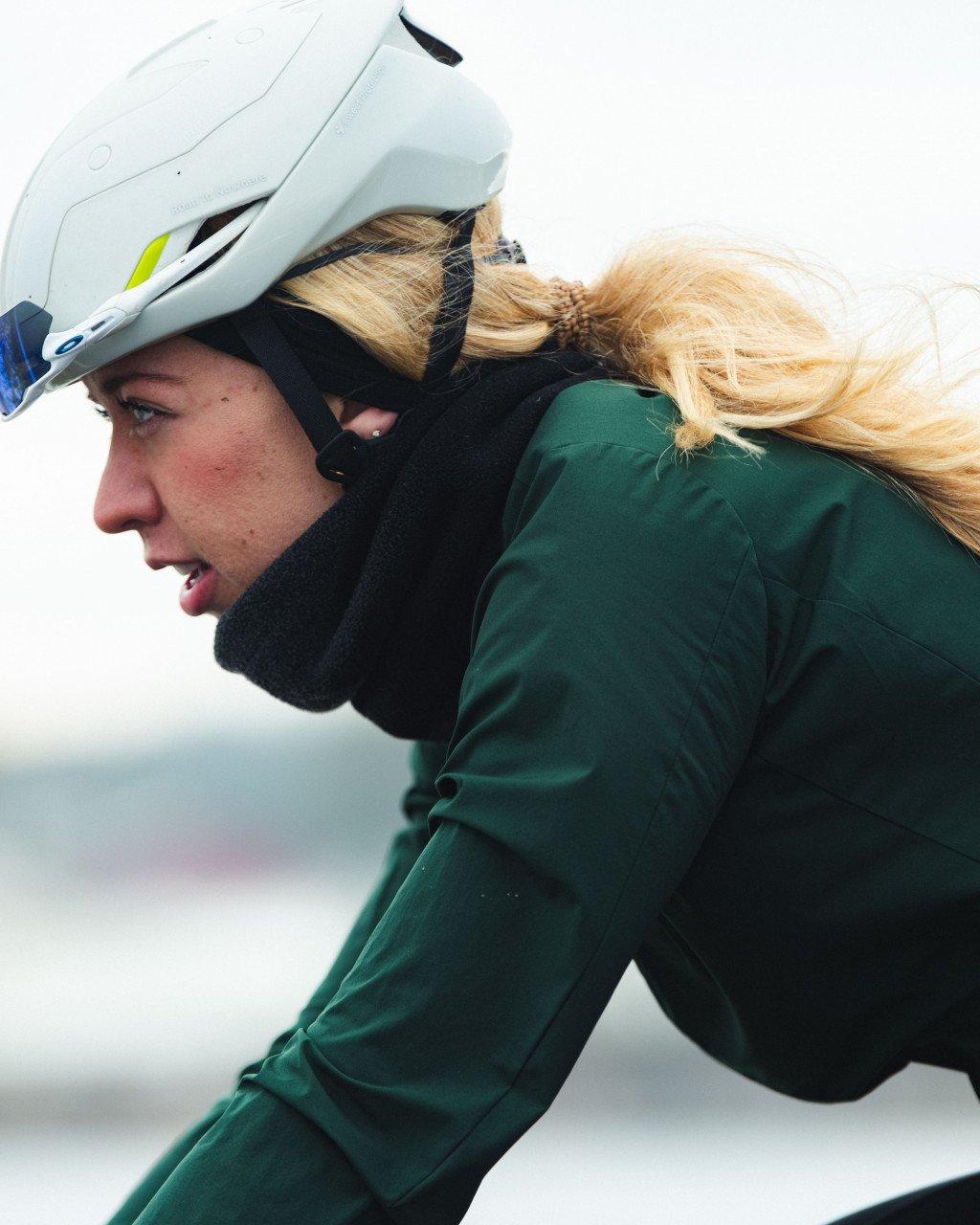 Model wearing green long-sleeve jersey and white cycling helmet in profile during winter ride