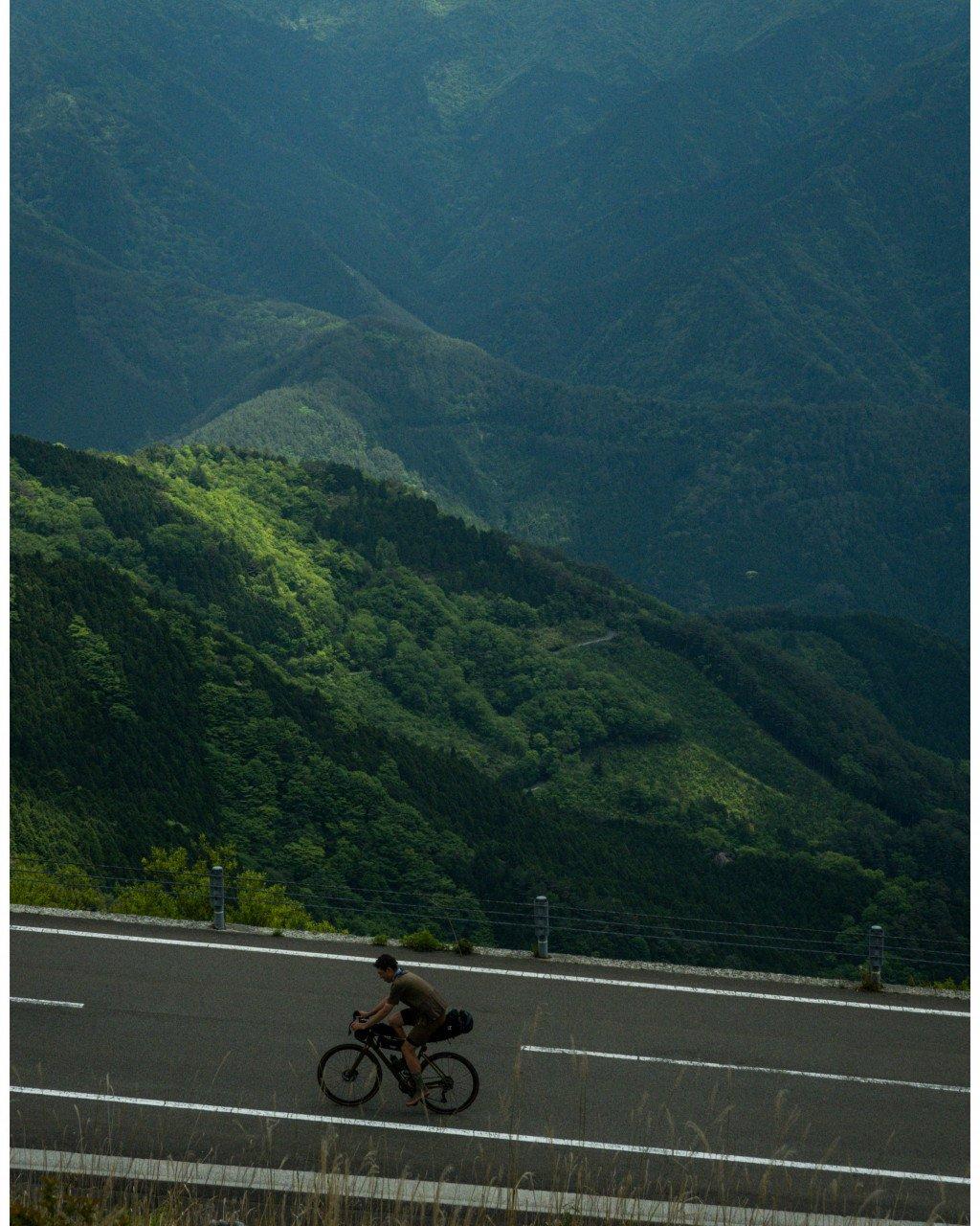 Cyclist riding through mountainous landscape with lush green hills and misty peaks