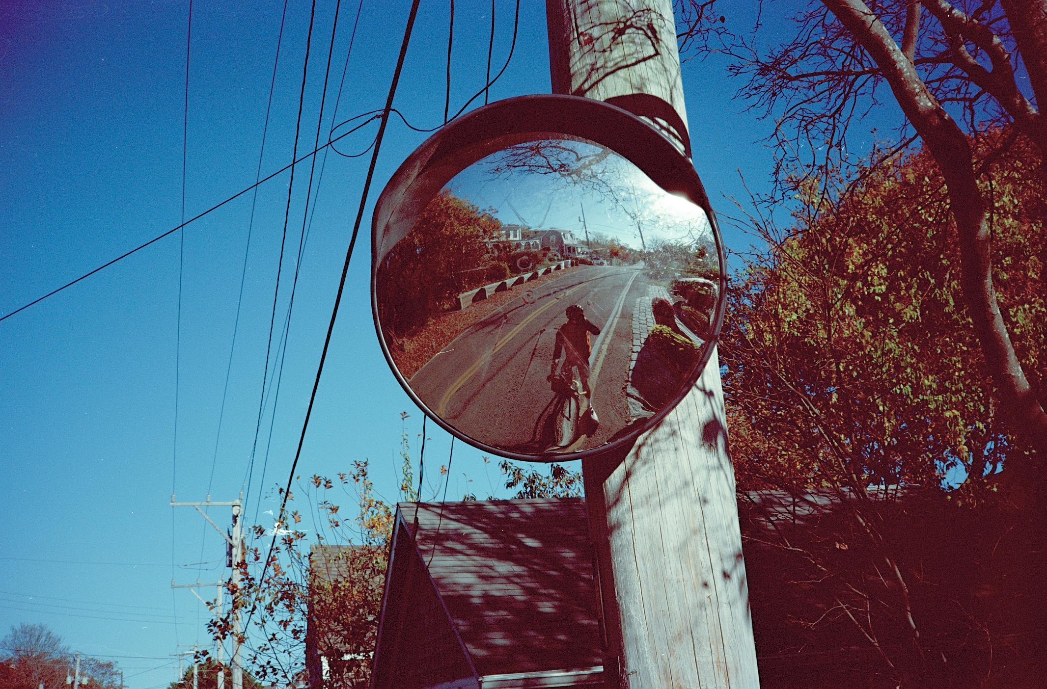 Cyclist reflected in curved roadside mirror on rural road with autumn trees
