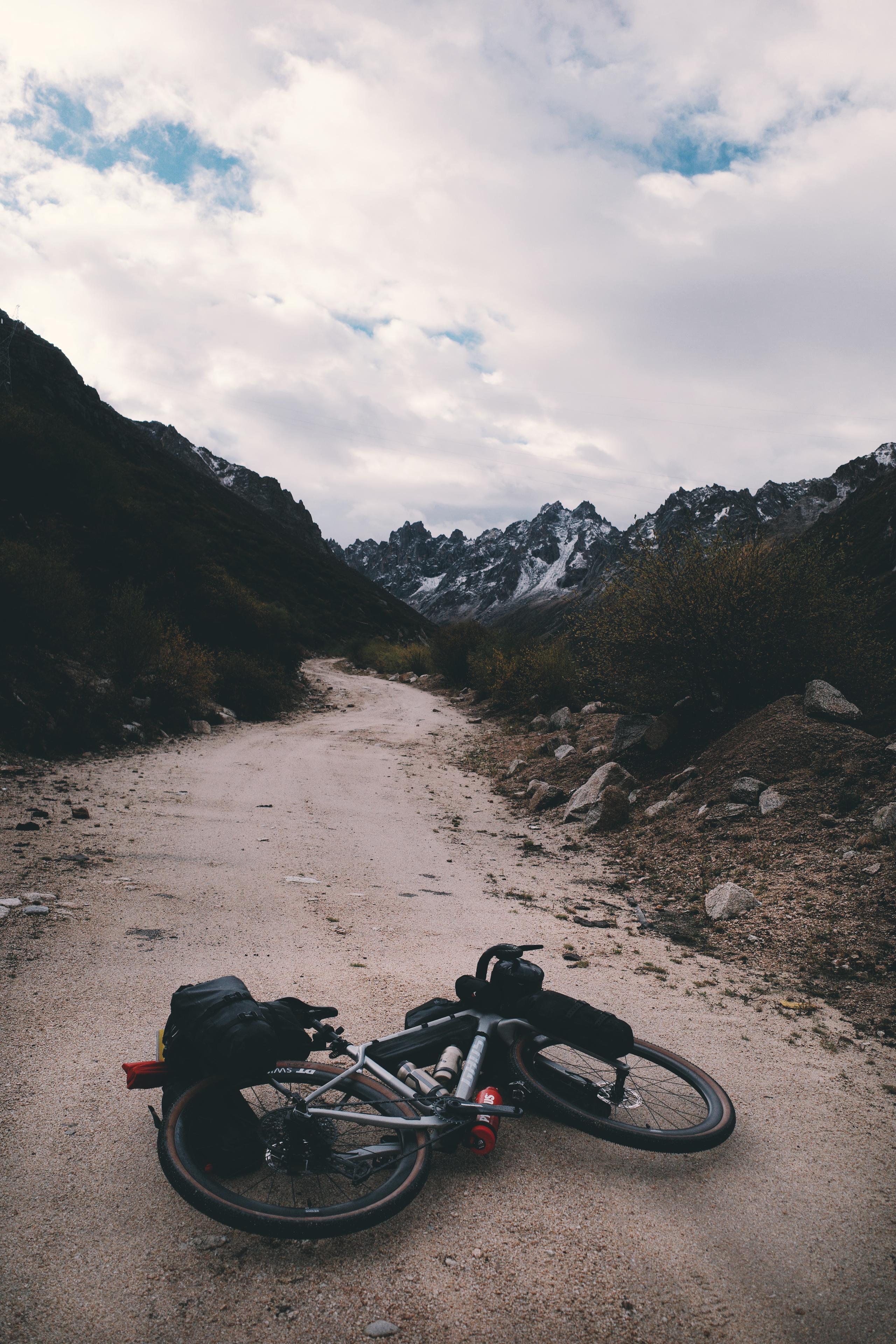 Bikepacking bicycle with bags on mountain gravel road with snow-capped peaks in background