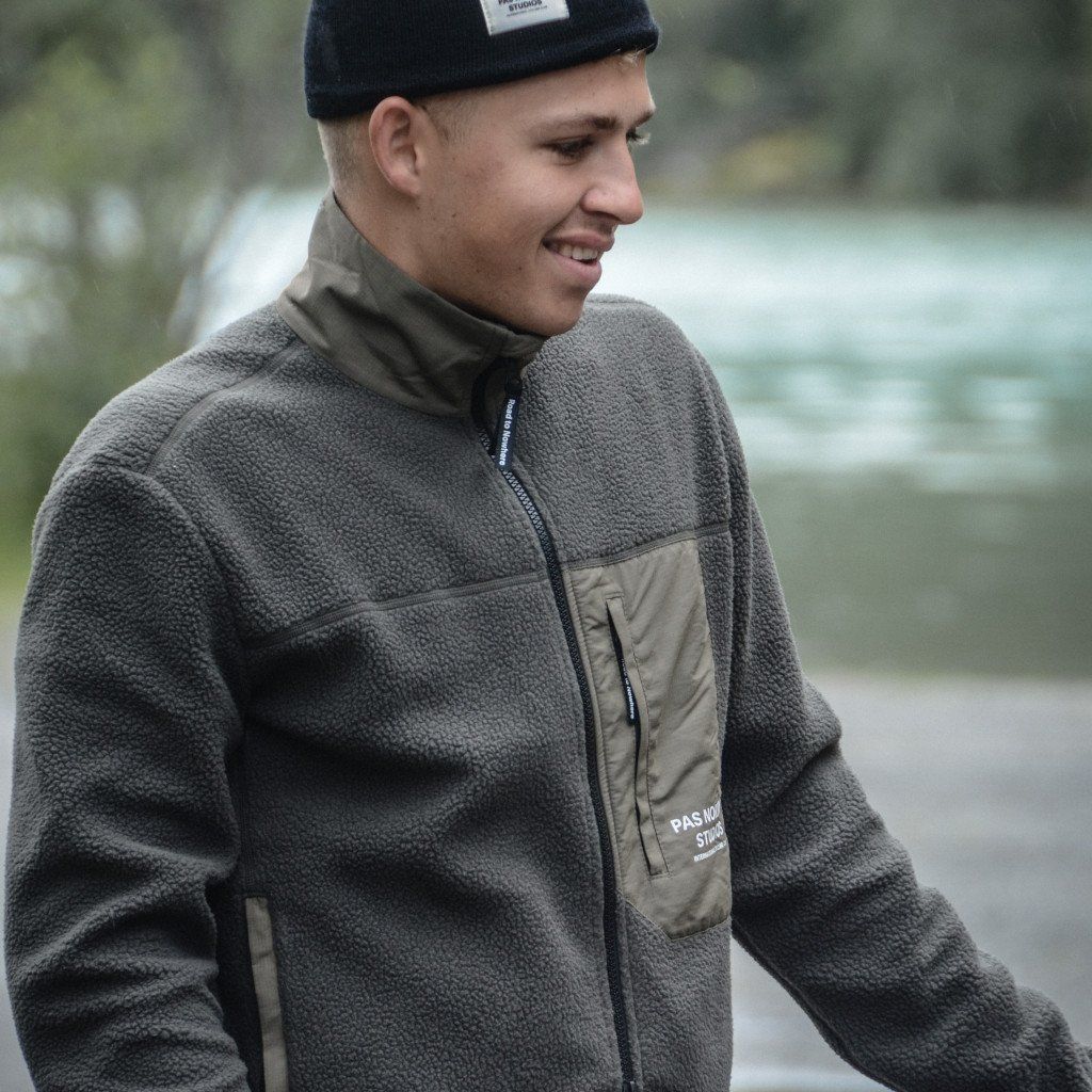 Model wearing grey fleece jacket with contrasting panels and black beanie outdoors