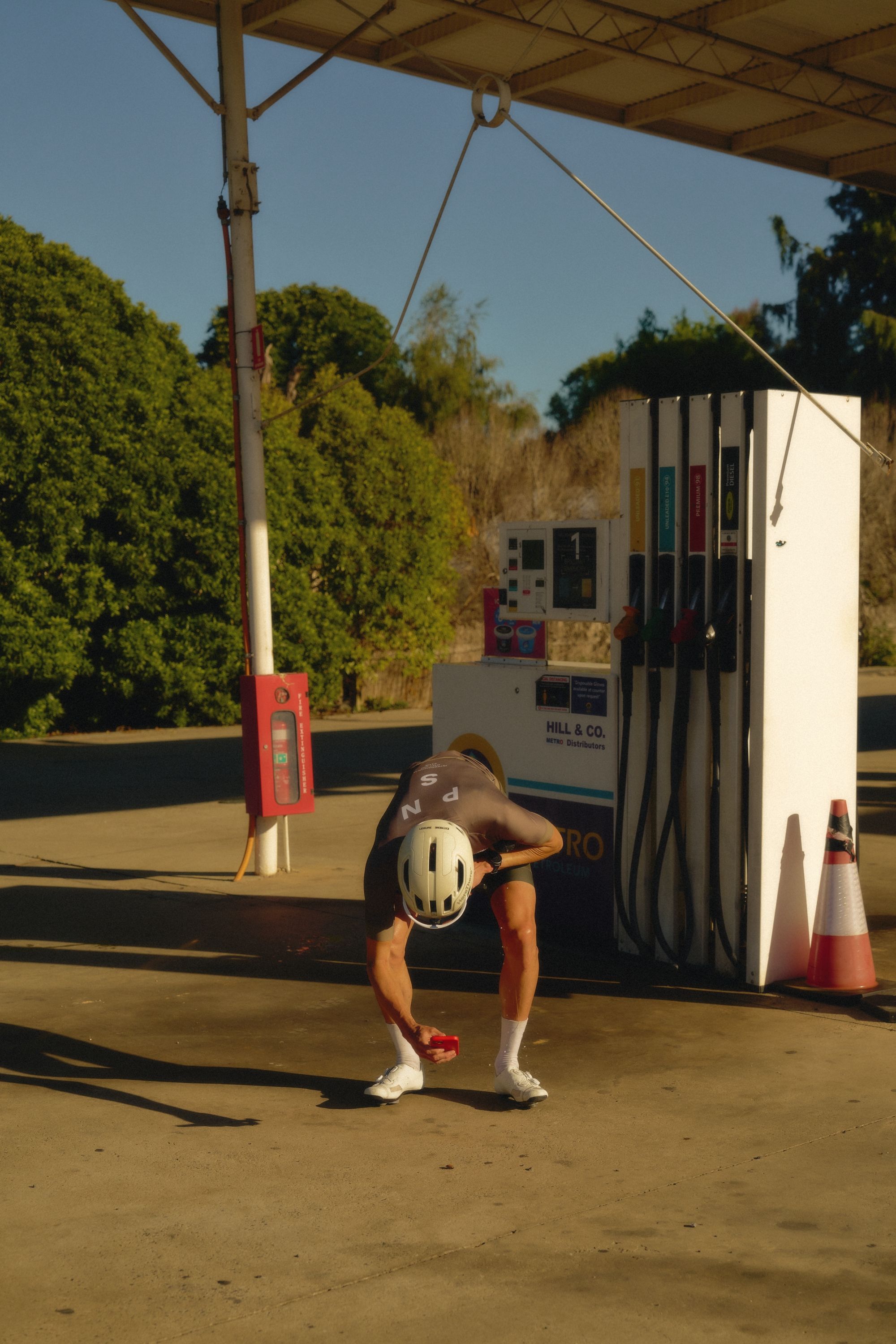 Model wearing cycling kit with helmet, leaning forward at gas station
