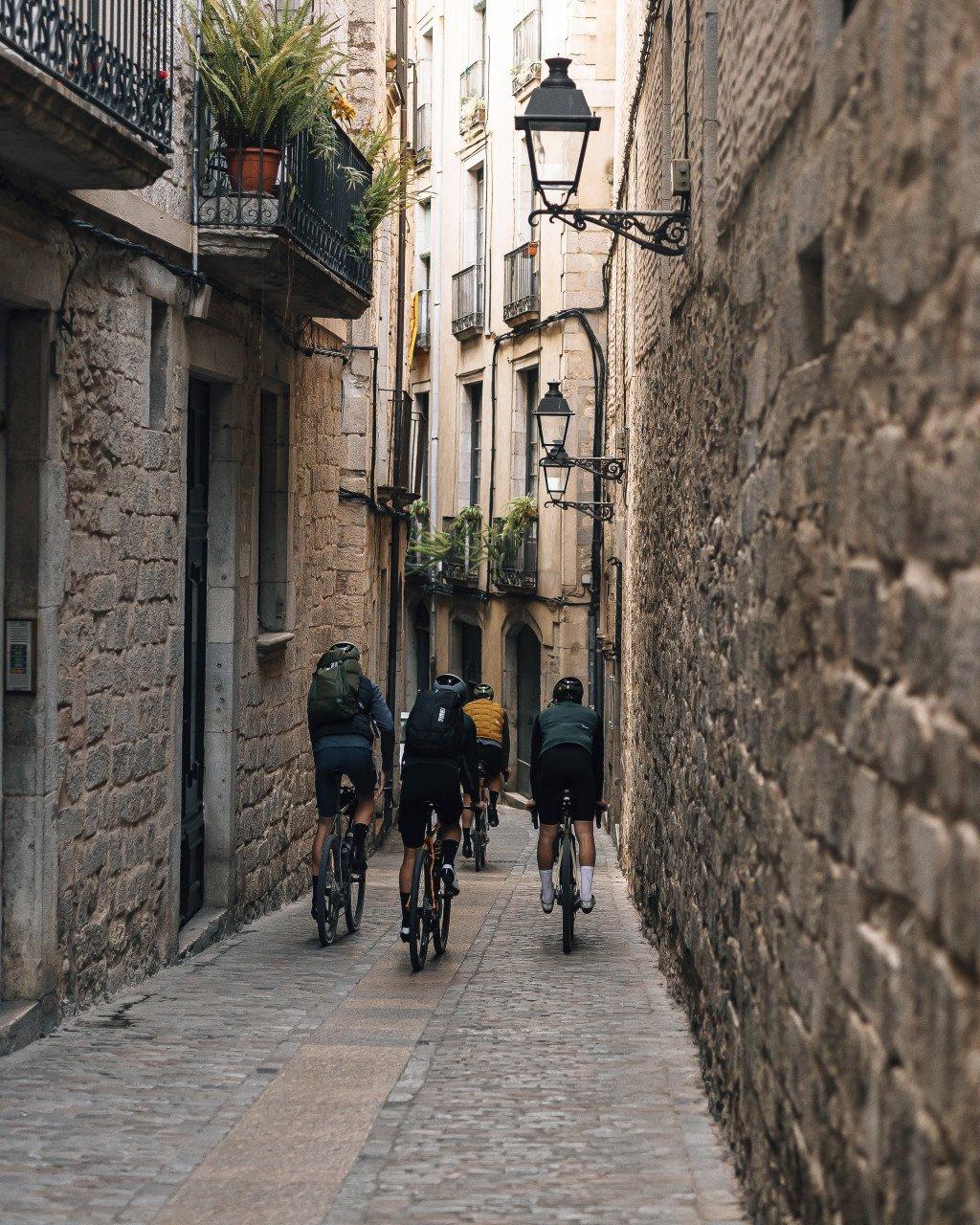 Cyclists riding through narrow cobblestone street in historic town with stone buildings and lanterns