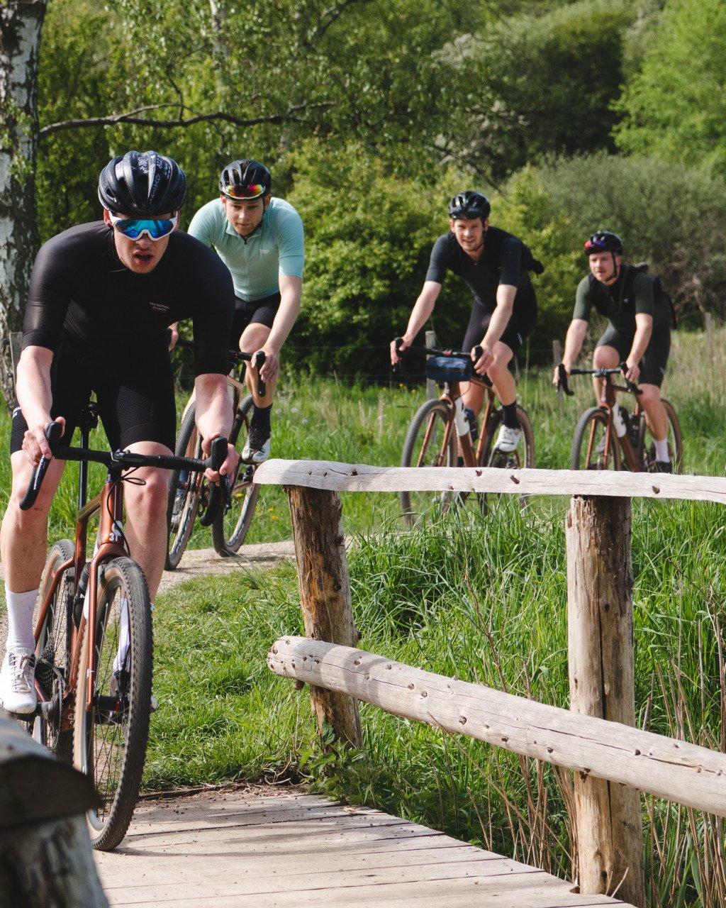 Cyclists in aerodynamic gear riding time trial bikes on rural path with wooden fence