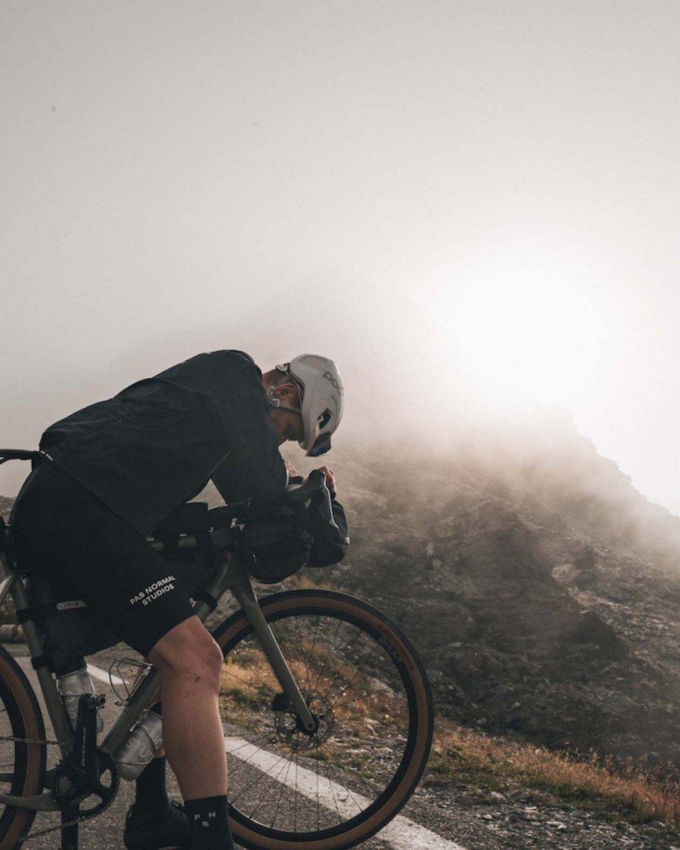 Cyclist in dark jersey and helmet riding through misty mountain terrain at sunrise