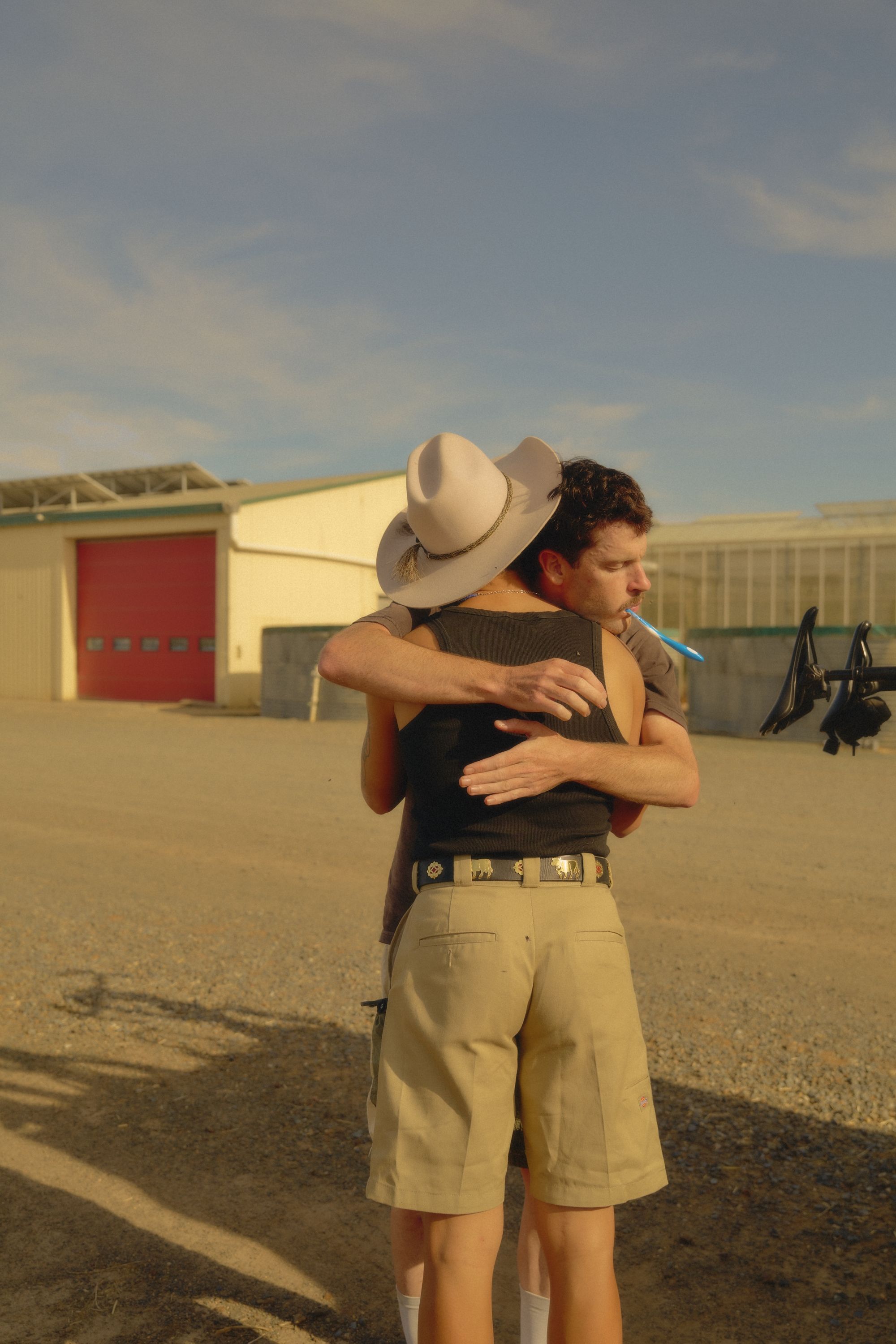 Two men embracing outdoors in casual clothing with desert buildings in background