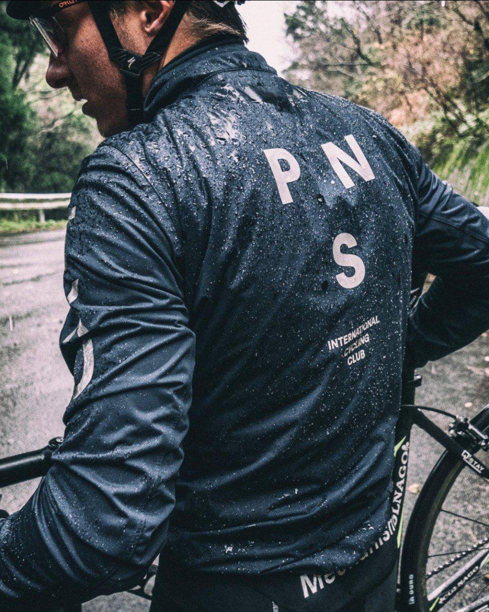 Model wearing navy cycling jacket with water droplets and back lettering on road