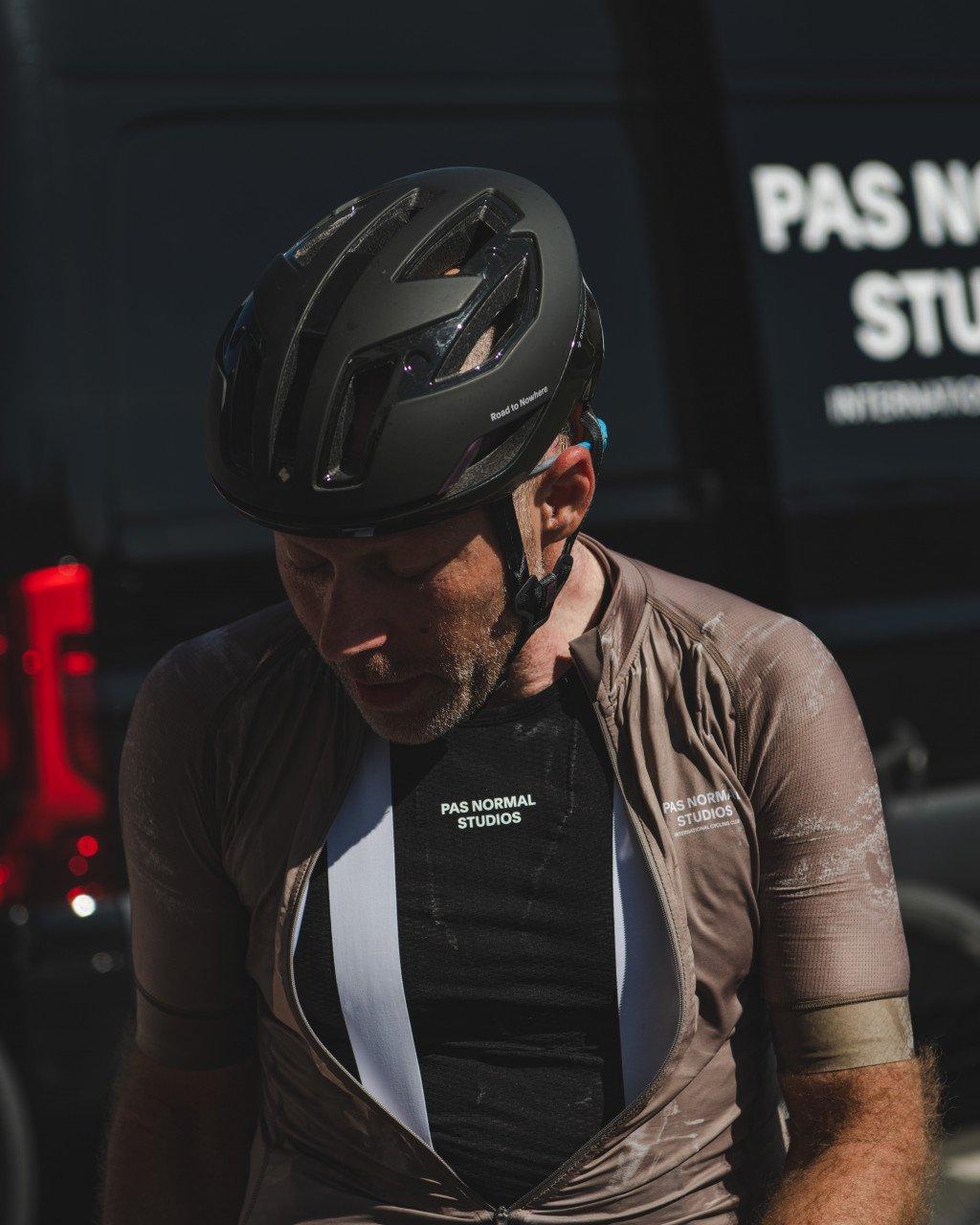 Model wearing black cycling helmet and brown base layer with chest branding in dim lighting