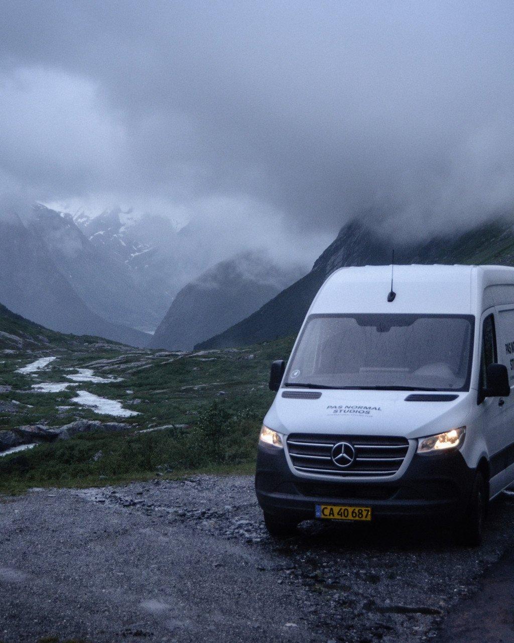 White Mercedes van with logo branding parked on mountain road with misty peaks in background